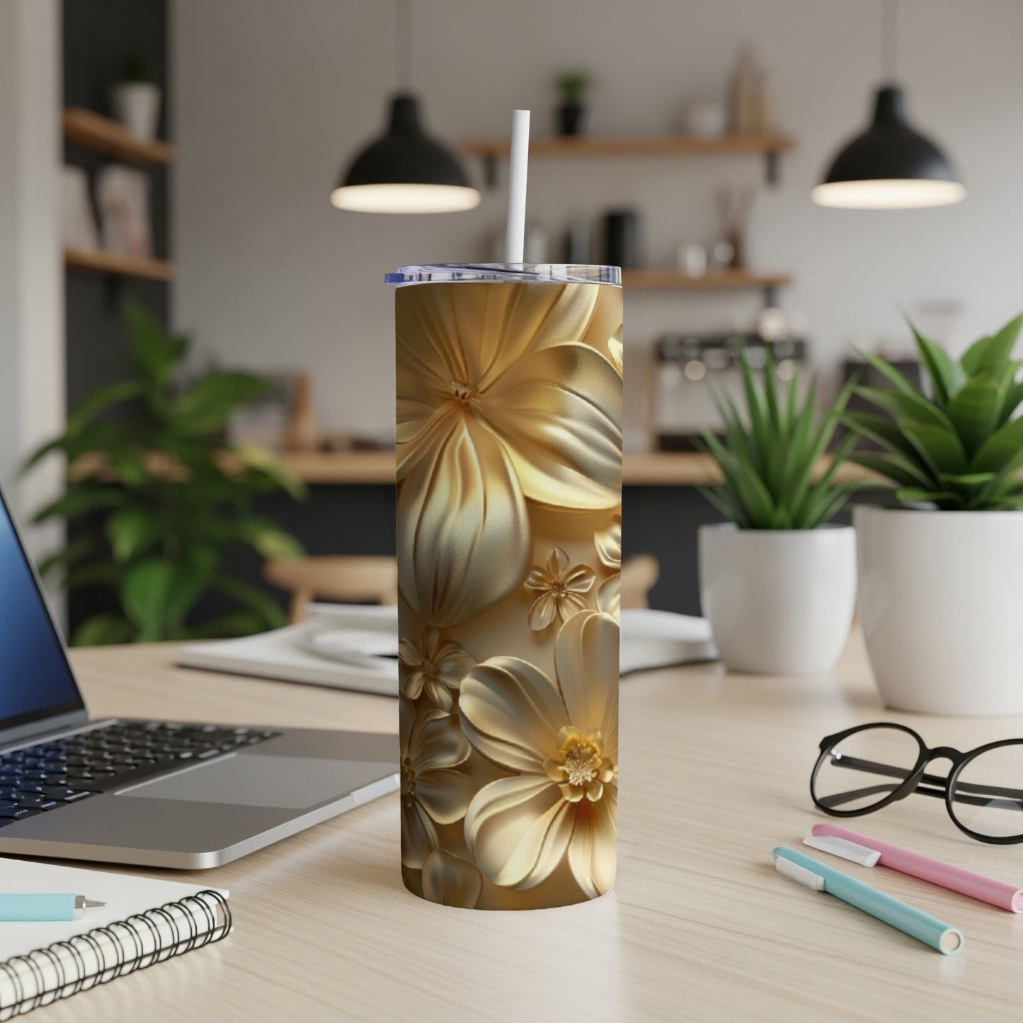 Gold floral patterned tumbler with straw on a desk.