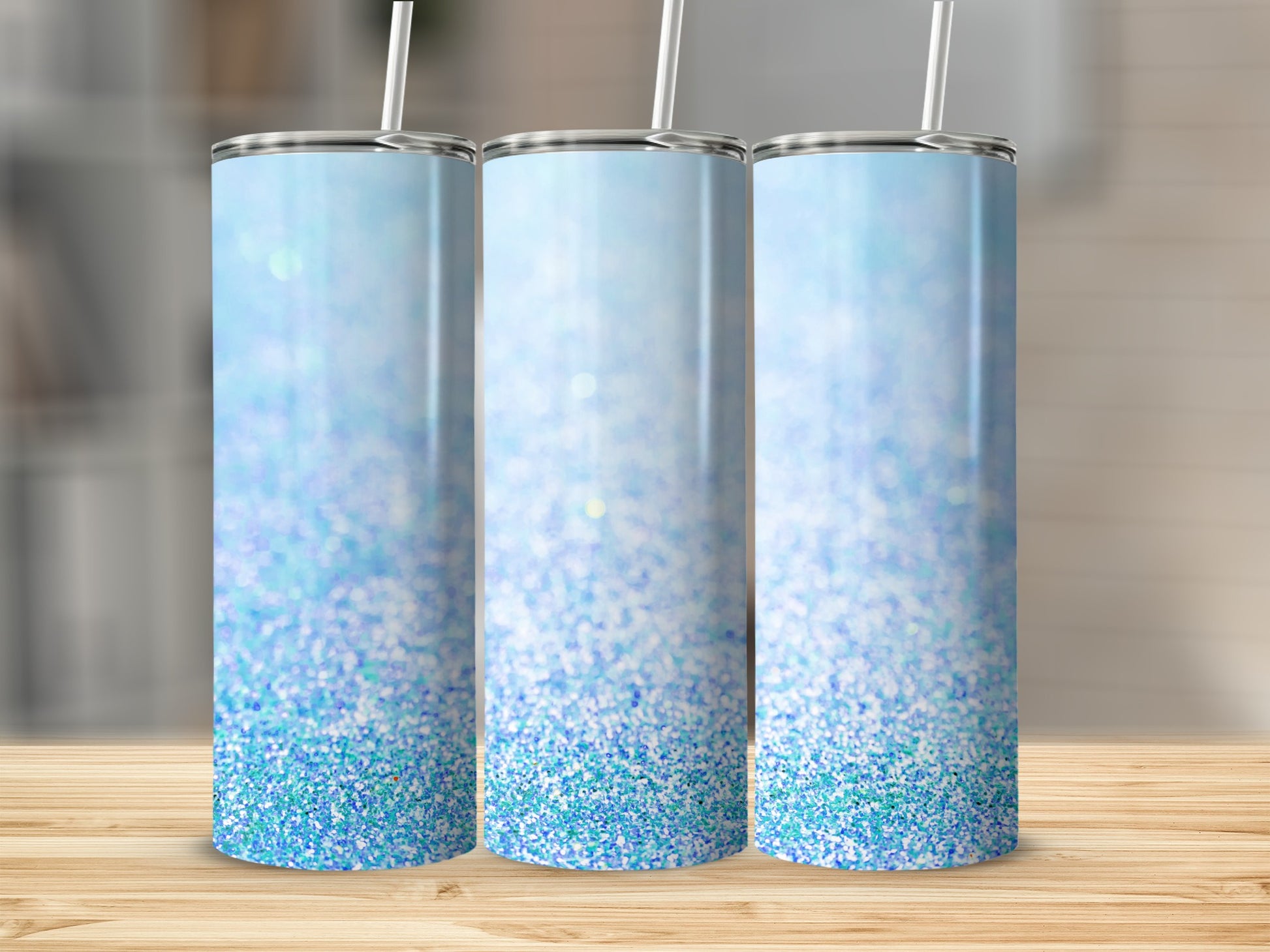 Three blue glitter tumblers with straws stand on a wooden surface.