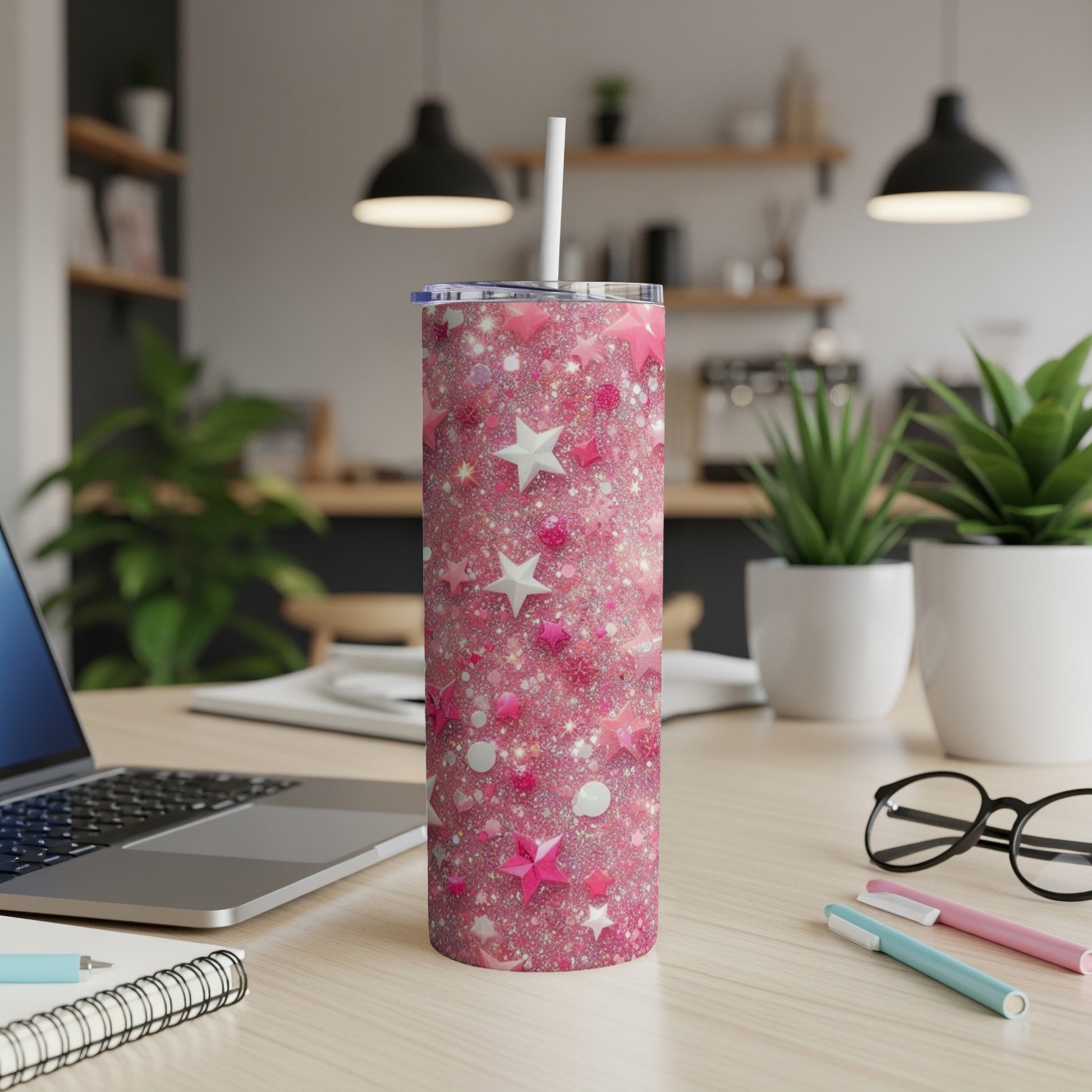 Pink glitter tumbler with stars, circles, and hearts, on a desk.