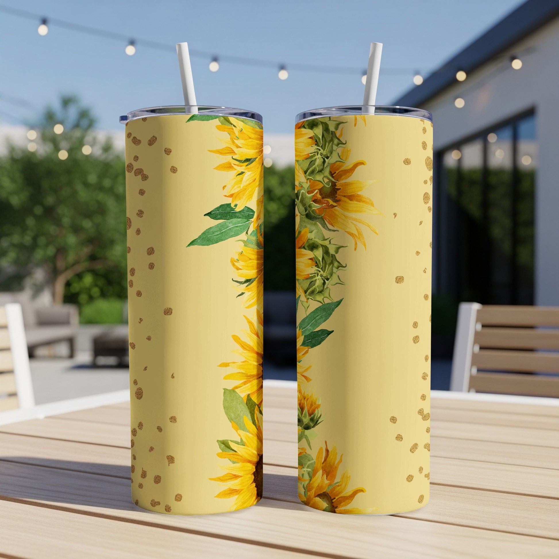 Two yellow tumblers with sunflower and gold dot design on a patio table.