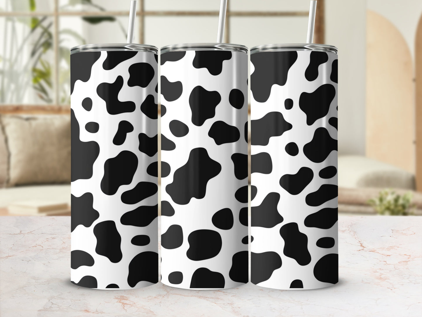 Three tumblers with a black and white cow print pattern, standing on a marble surface.