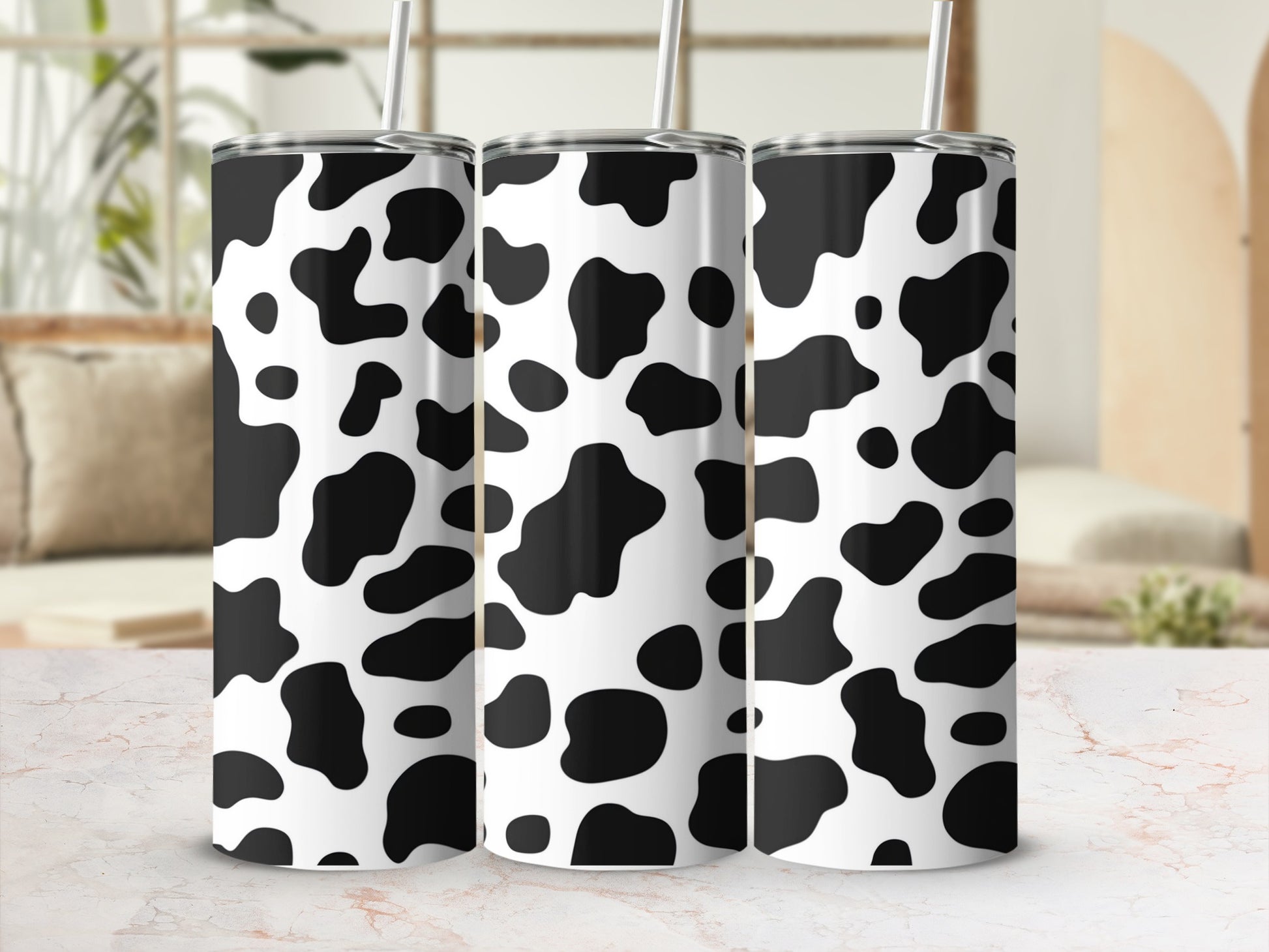Three tumblers with a black and white cow print pattern, standing on a marble surface.