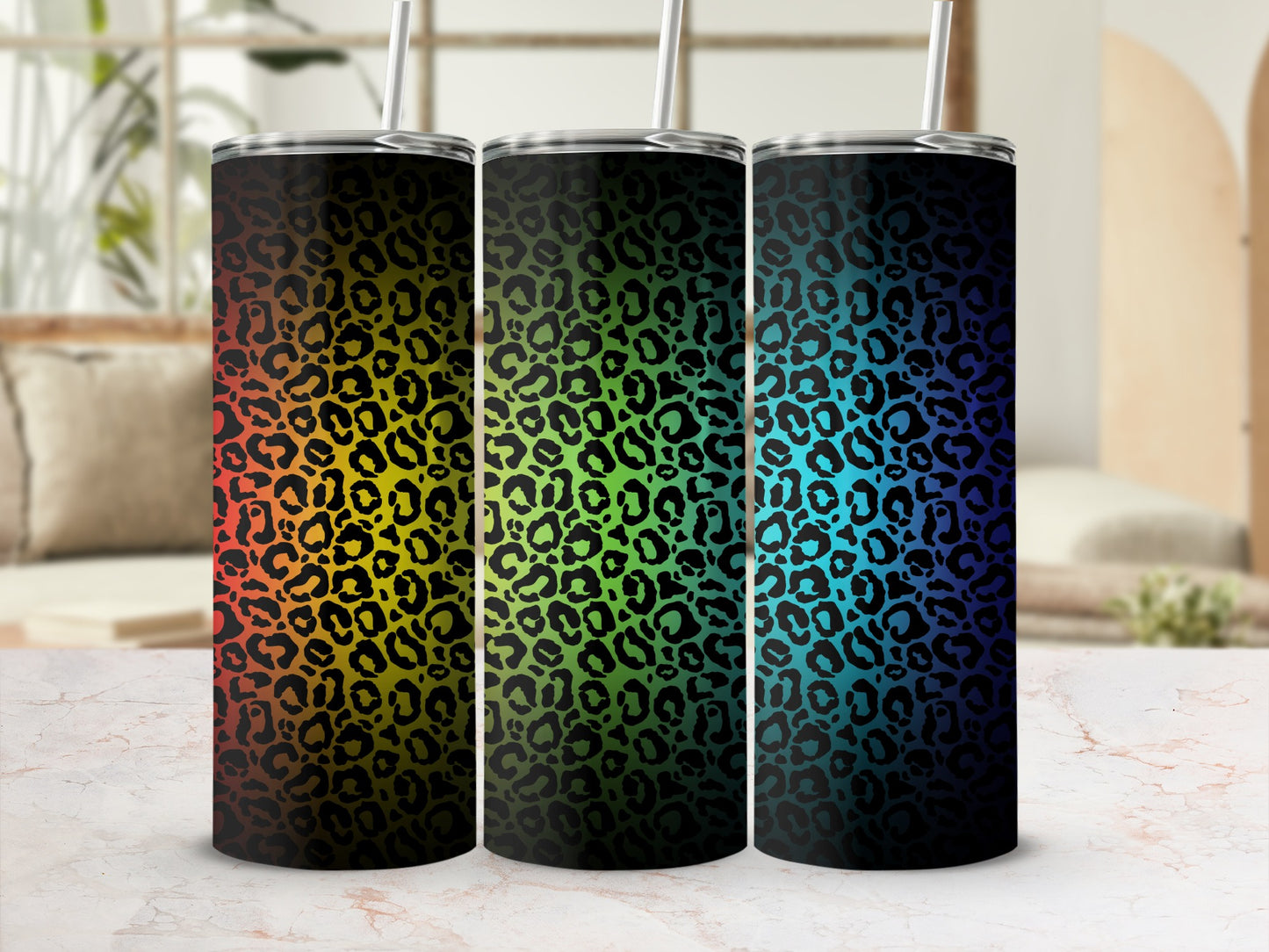 Three tumblers with rainbow and leopard print designs on a marble surface.