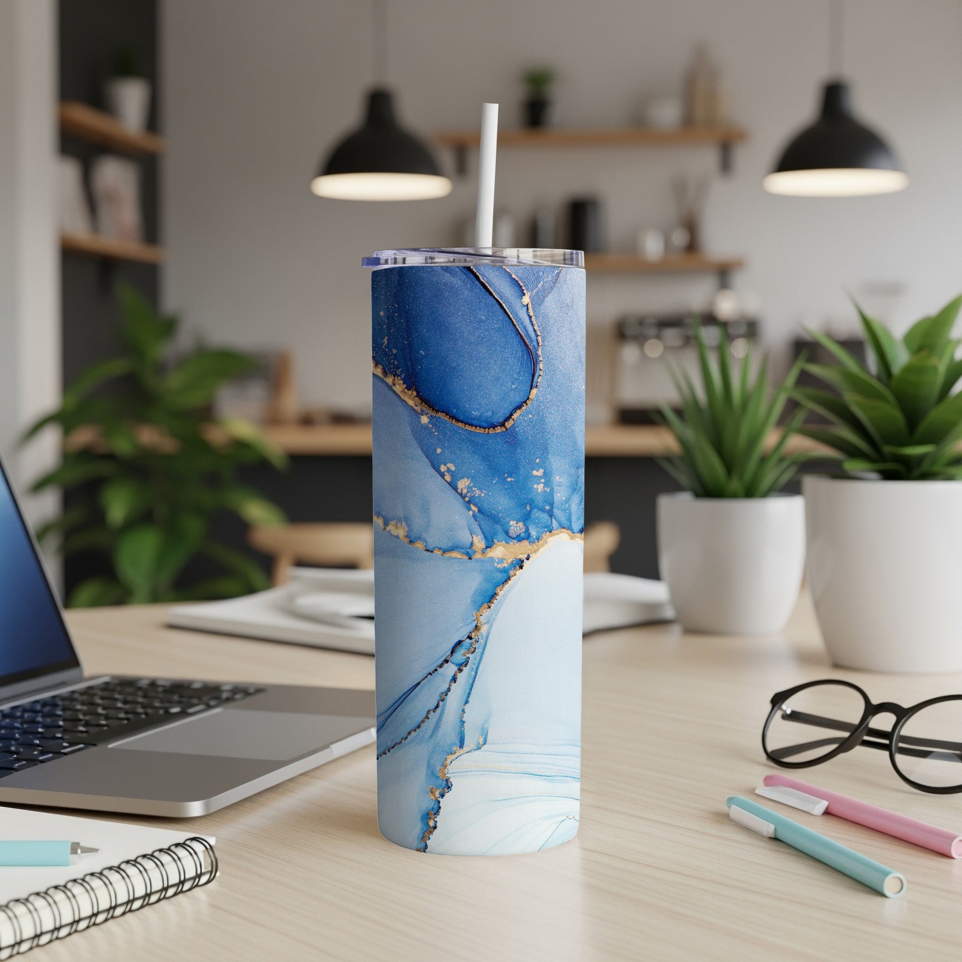 Blue and gold abstract art tumbler with straw on desk.