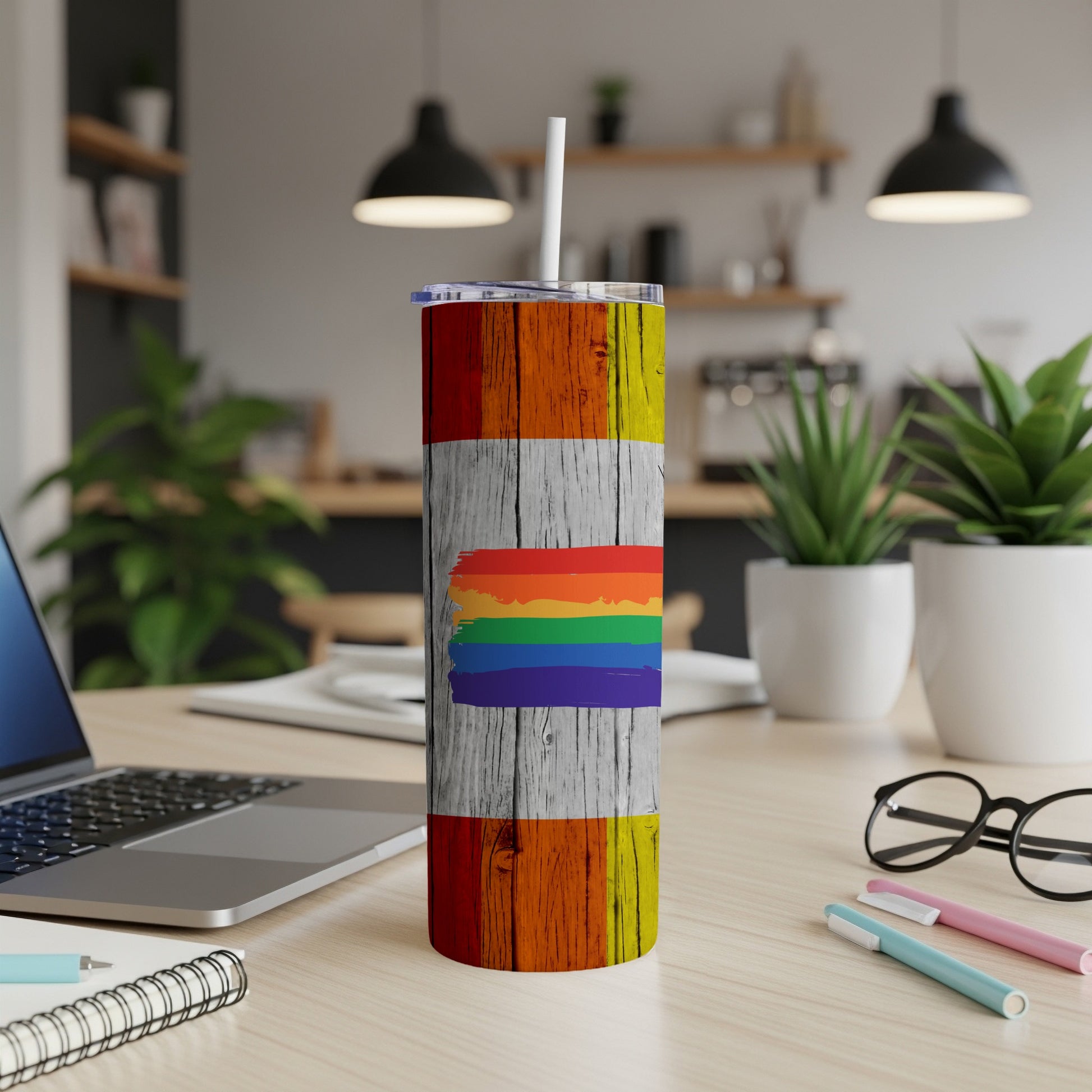 Rainbow flag tumbler on a desk next to a laptop and pens.