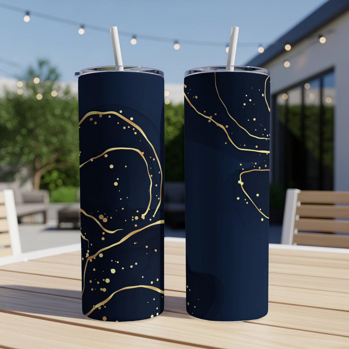 Two dark blue tumblers with gold abstract swirl and speckle patterns on an outdoor table.