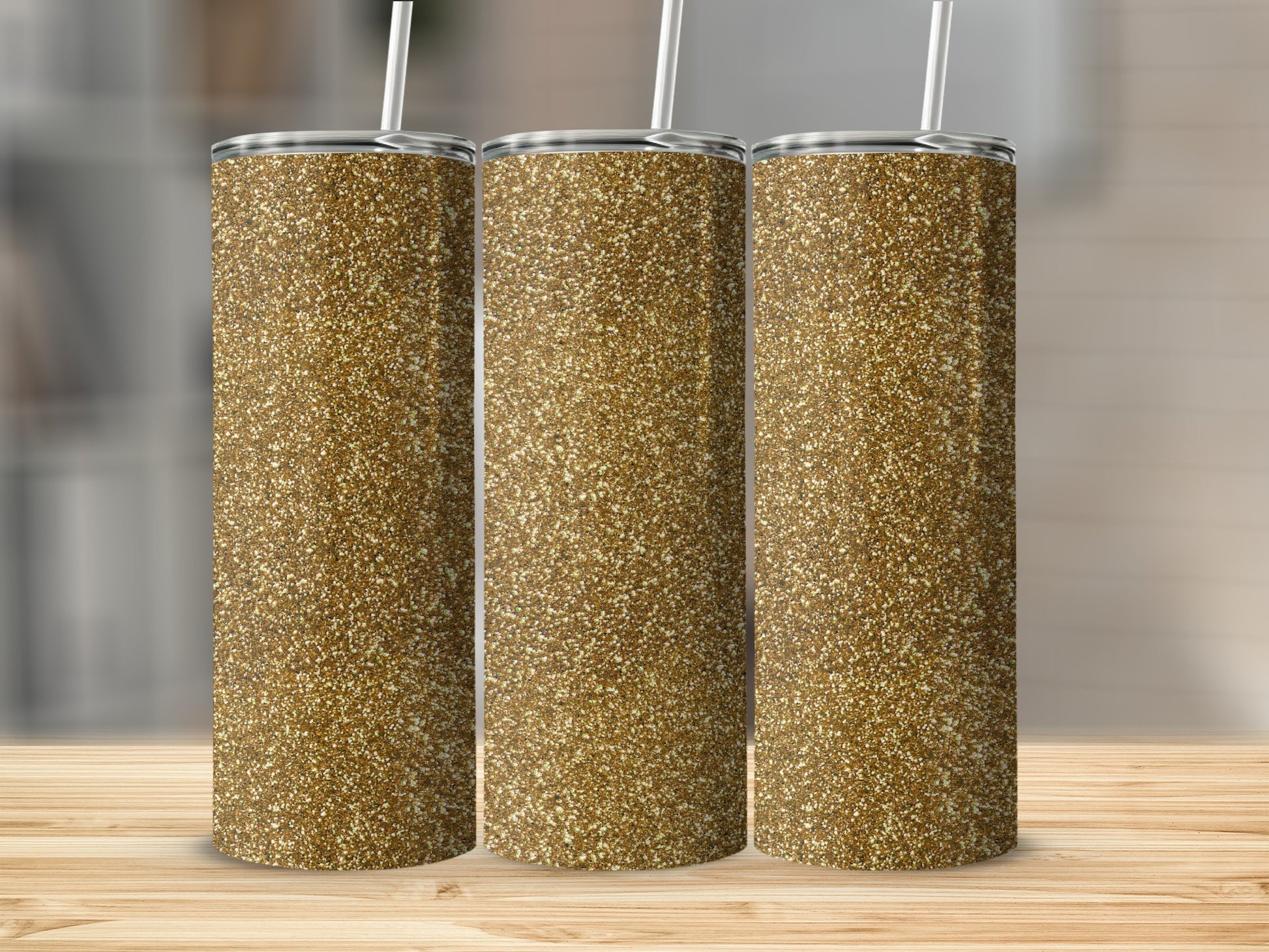 Three gold glitter tumblers with straws on a wooden surface.