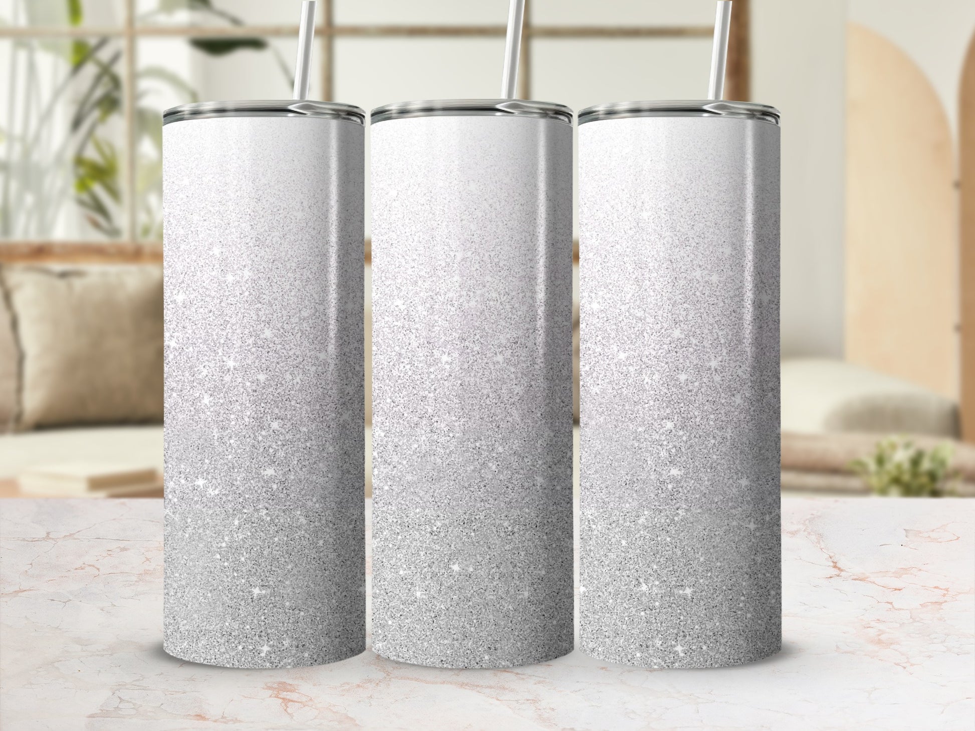 Three silver glitter tumblers with straws on a marble surface.