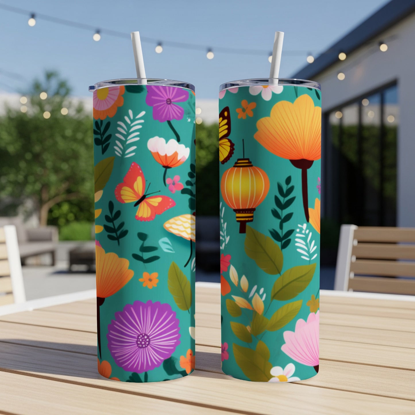 Two teal tumblers with floral, butterfly, and lantern pattern on outdoor table.