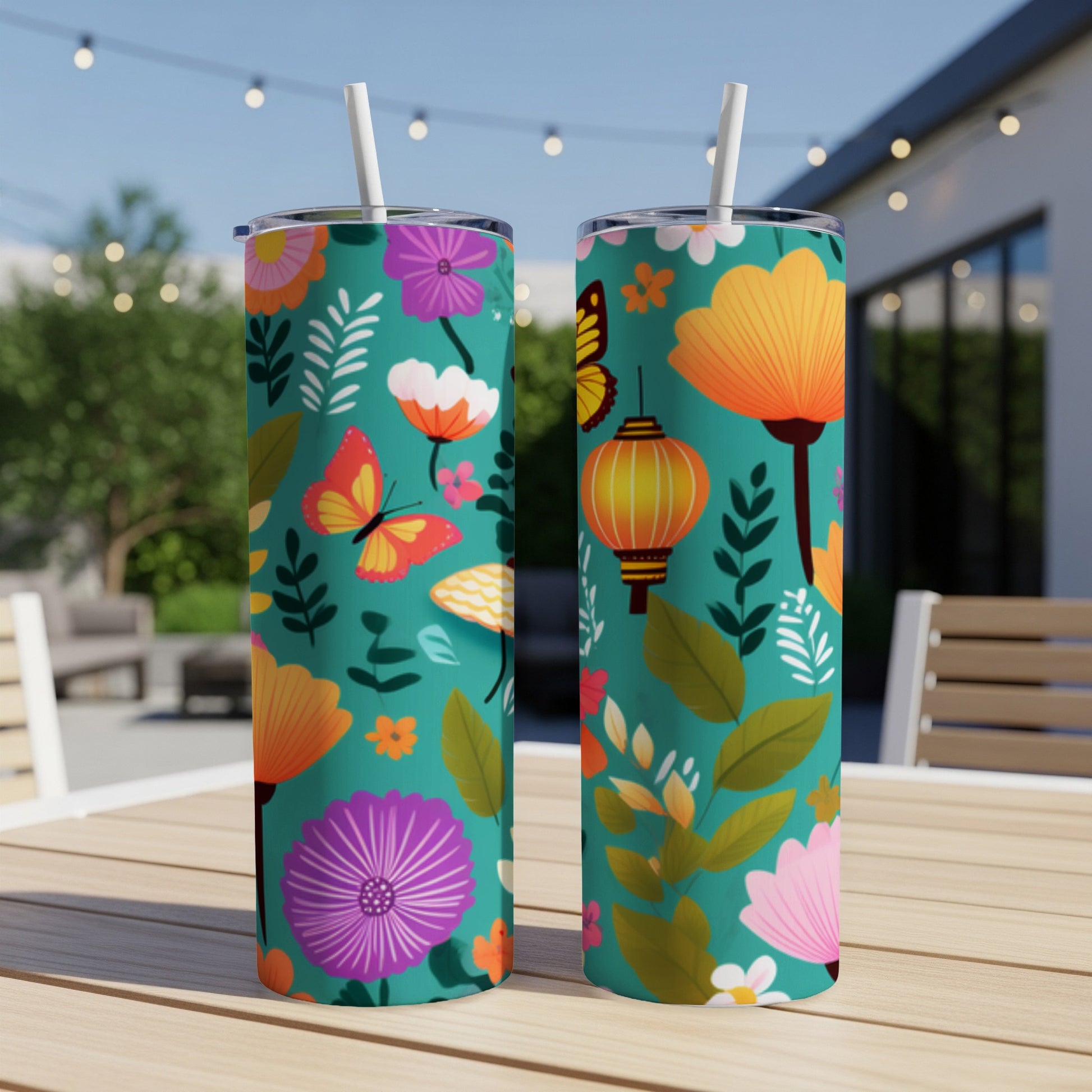 Two teal tumblers with floral, butterfly, and lantern pattern on outdoor table.