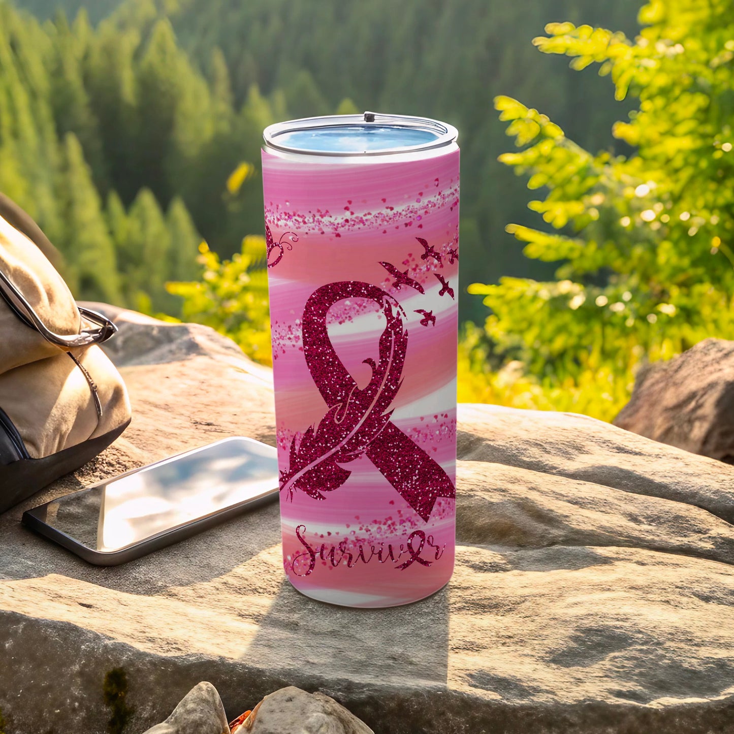 Pink glitter ribbon tumbler with "Survivor" text and birds, resting on rocks.
