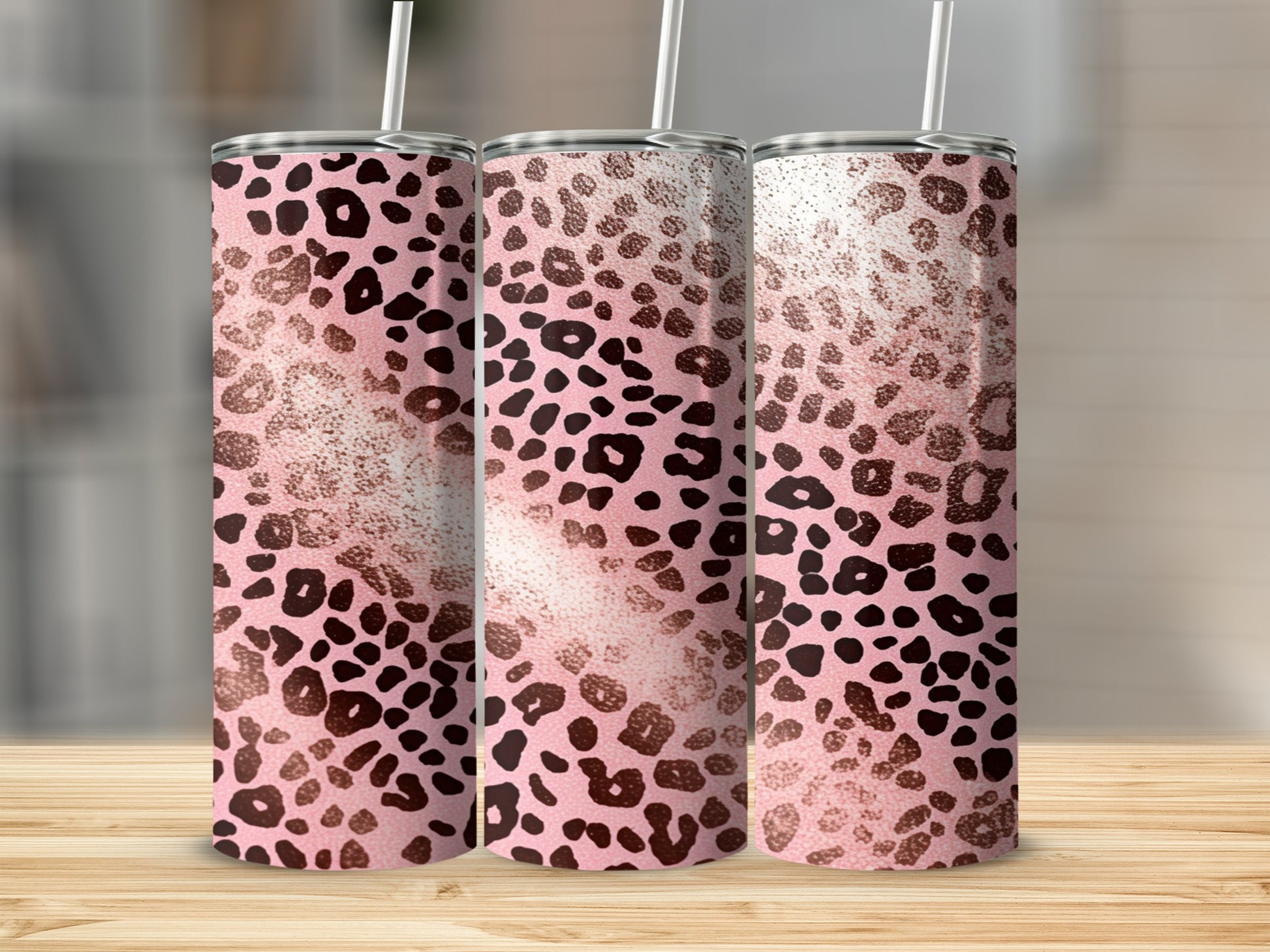 Three pink leopard print tumblers with straws on a wooden surface.