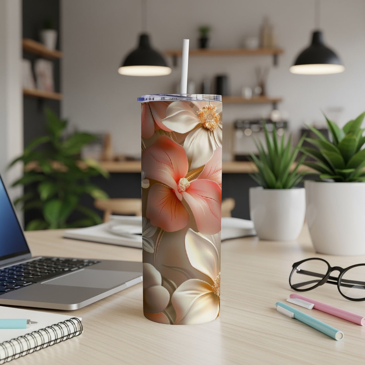 Floral tumbler with straw on a desk next to a laptop and pens.
