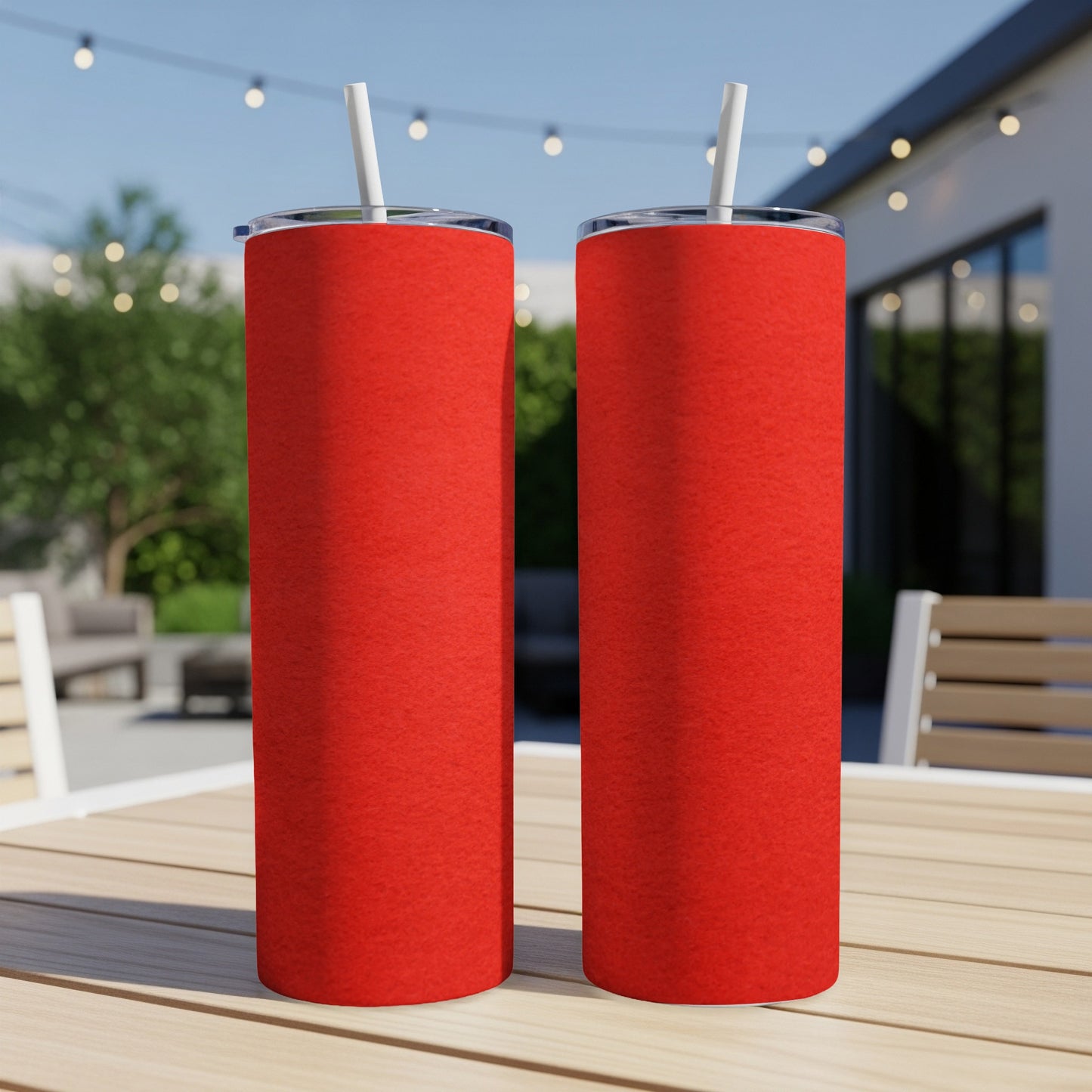 Two red tumblers with straws sit on a wooden table outdoors.