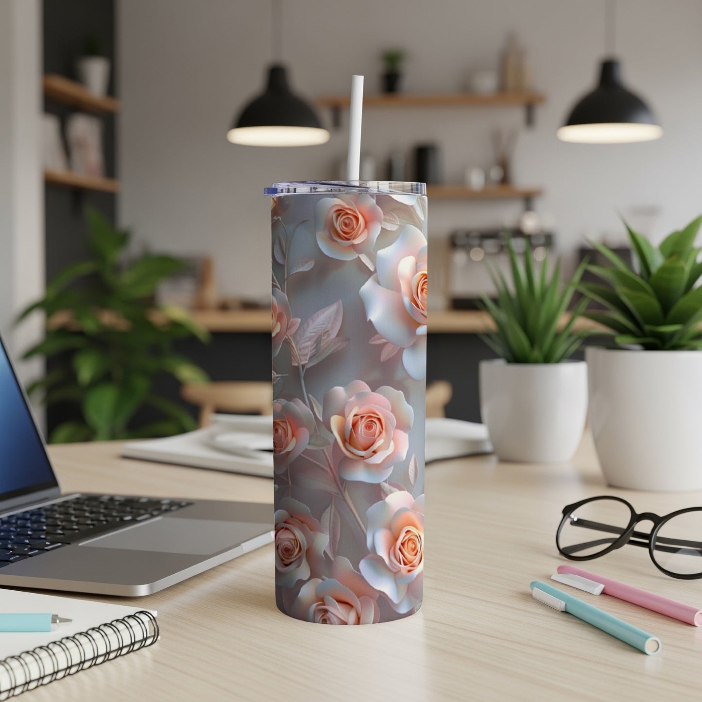 Tumbler with a pastel rose pattern on a desk with a laptop and pens.