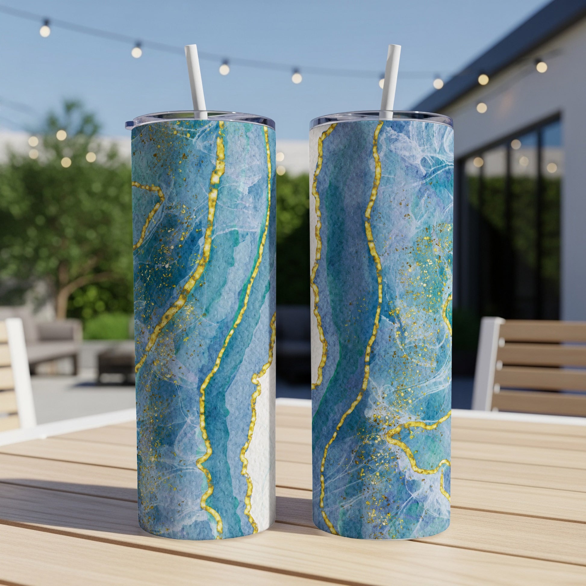Two blue and gold marbled tumblers with straws on a wooden table.