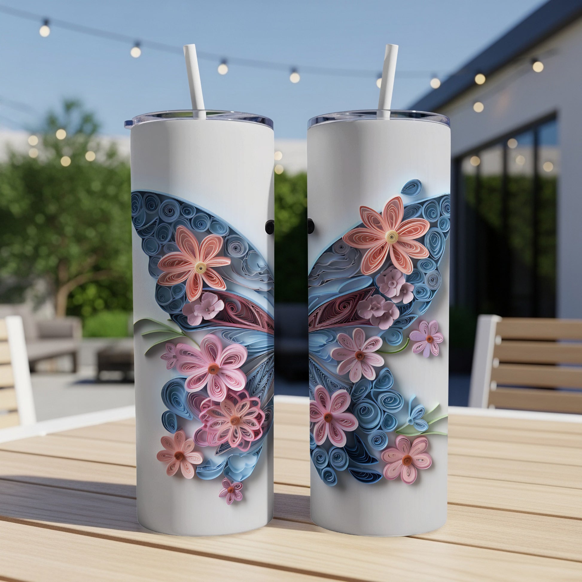 Two white tumblers with butterfly wing designs made of blue and pink quilled paper flowers.