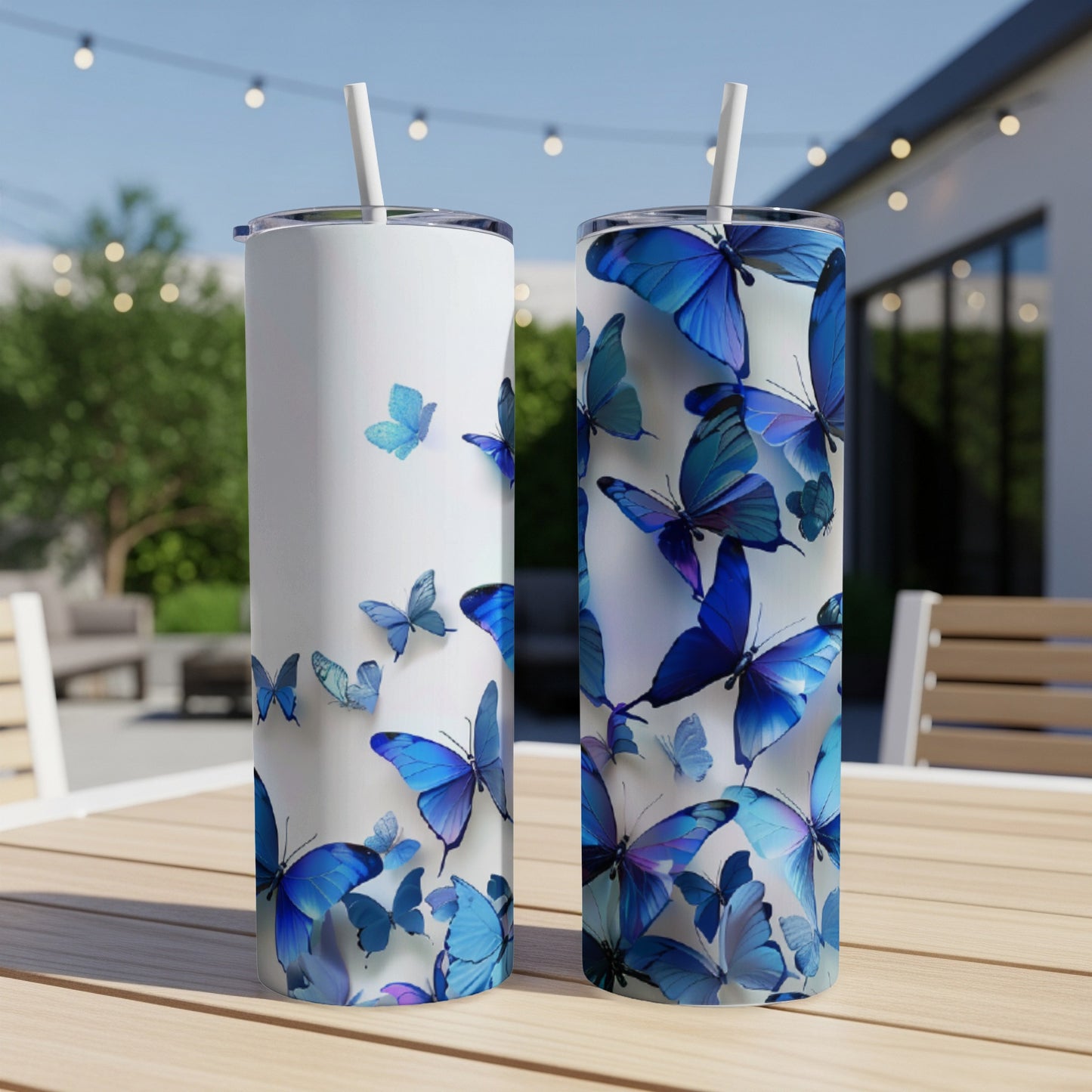 Two white tumblers with blue butterflies and straws on a table.