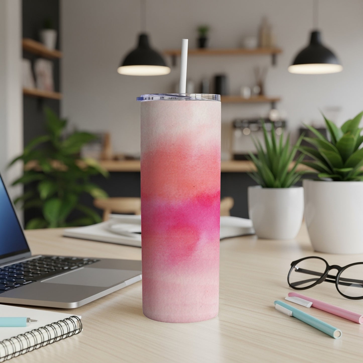Pink and red watercolor design tumbler with straw on desk.