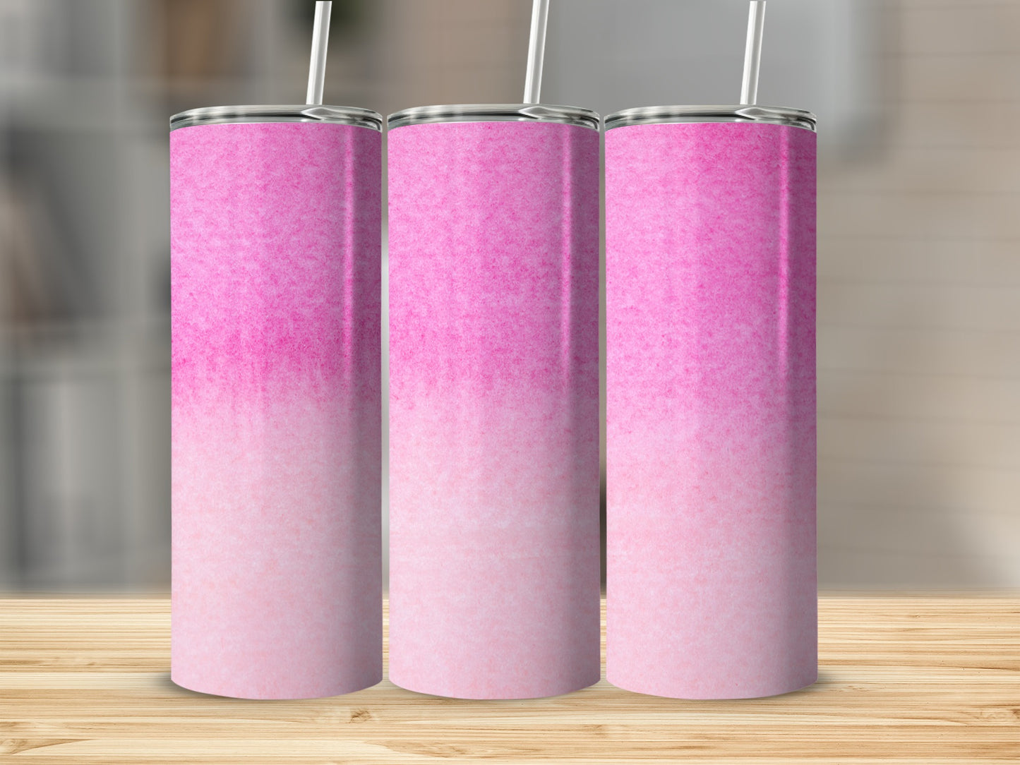 Three pink gradient tumblers with straws on a wooden surface.