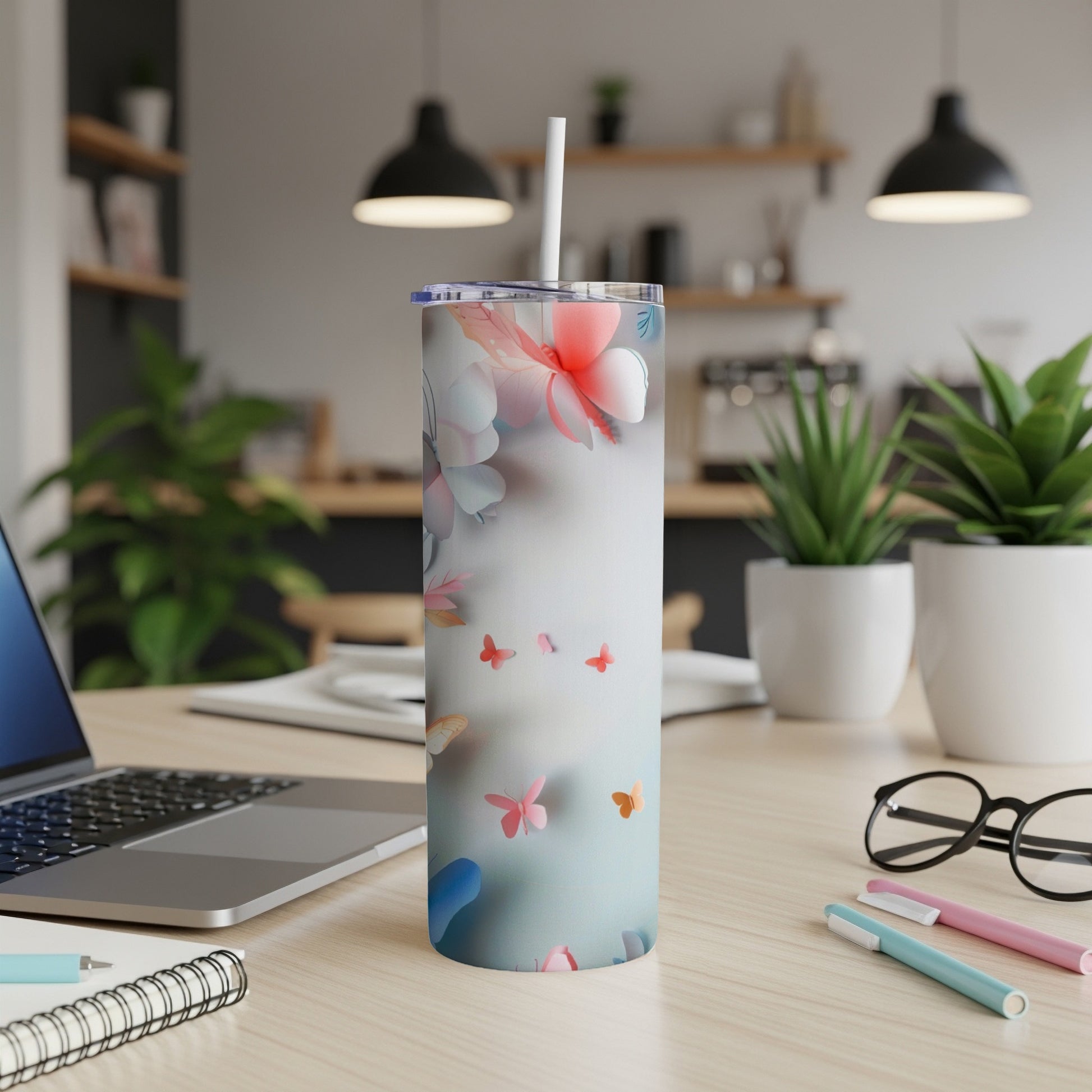 Floral tumbler with butterflies, straw, on a desk with laptop and pens.