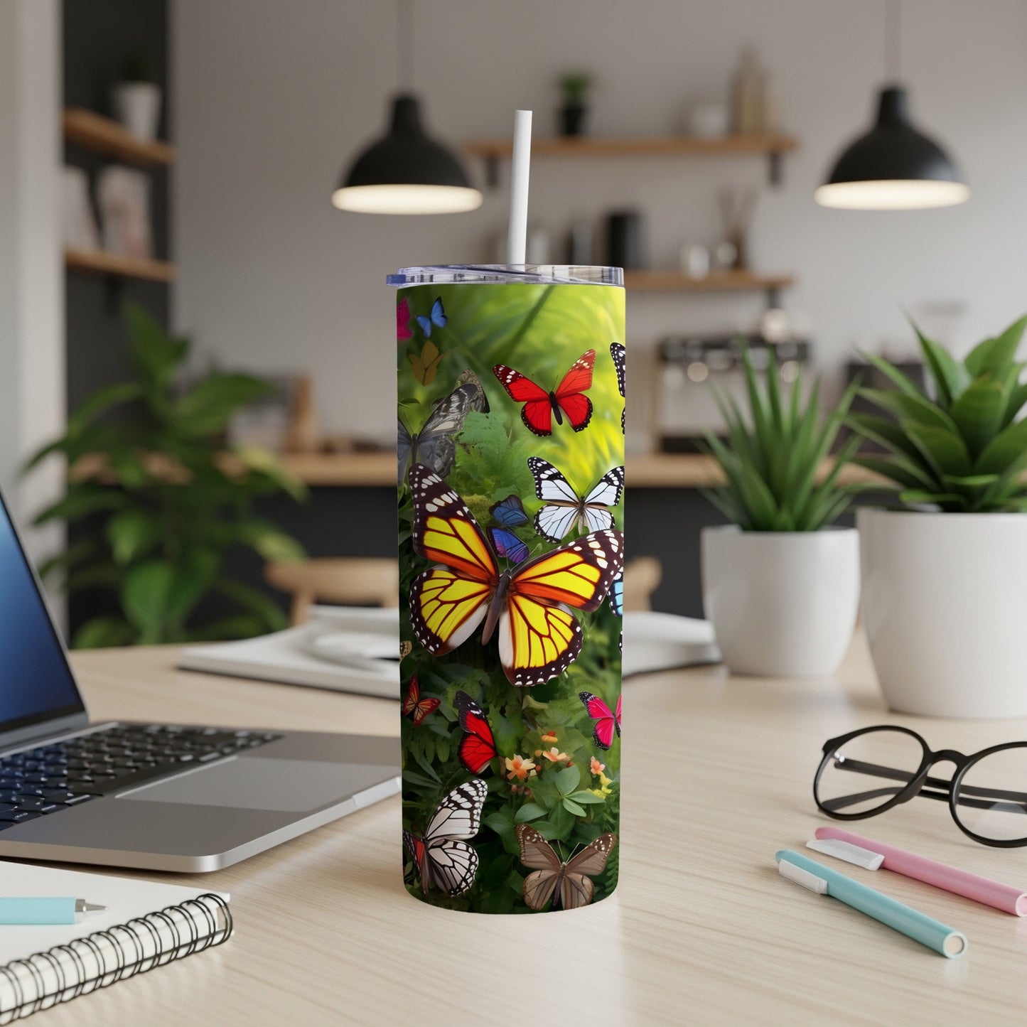 Tall tumbler with colorful butterflies, on a desk with a laptop and pens.
