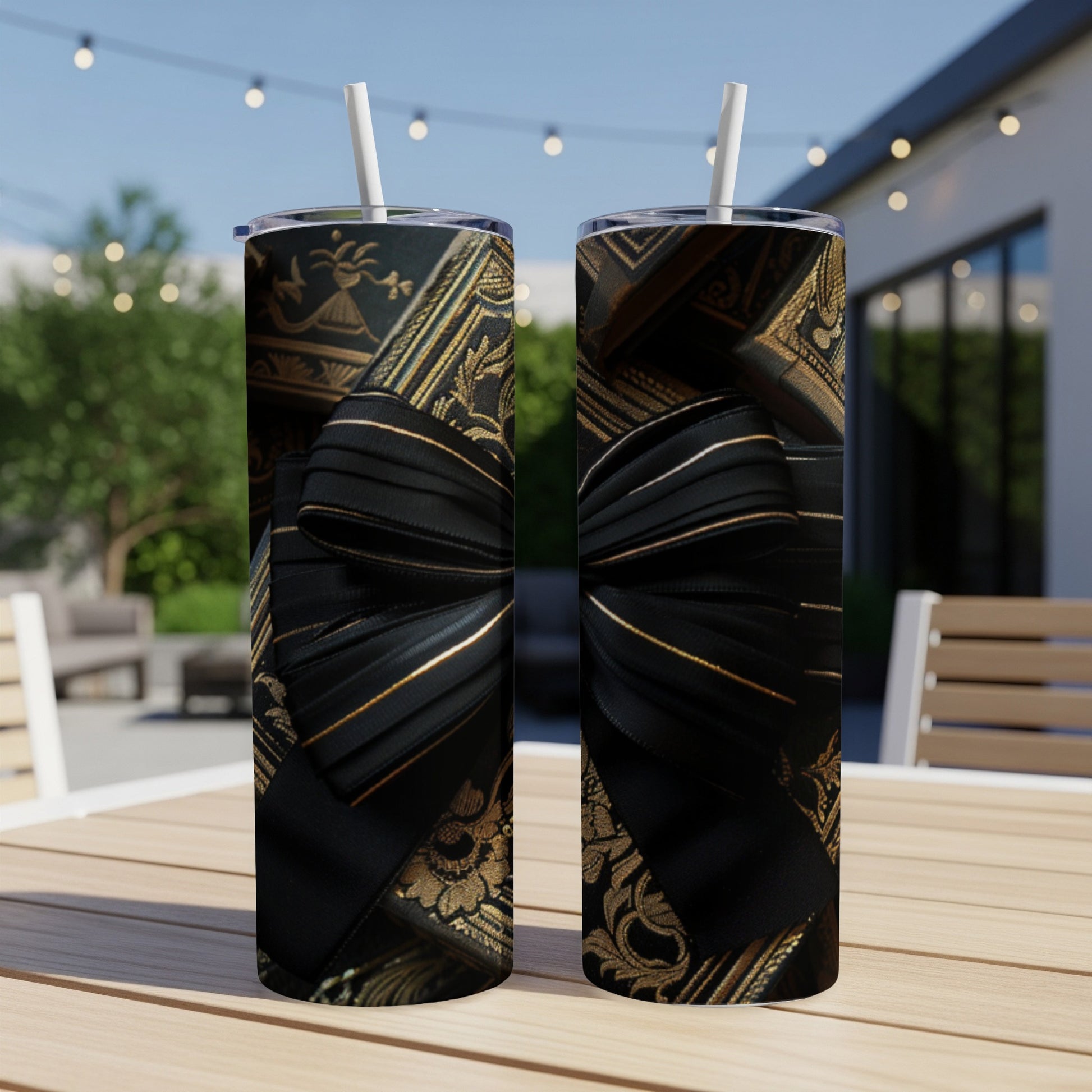 Two tumblers with black ribbon and gold ornate pattern on outdoor table.