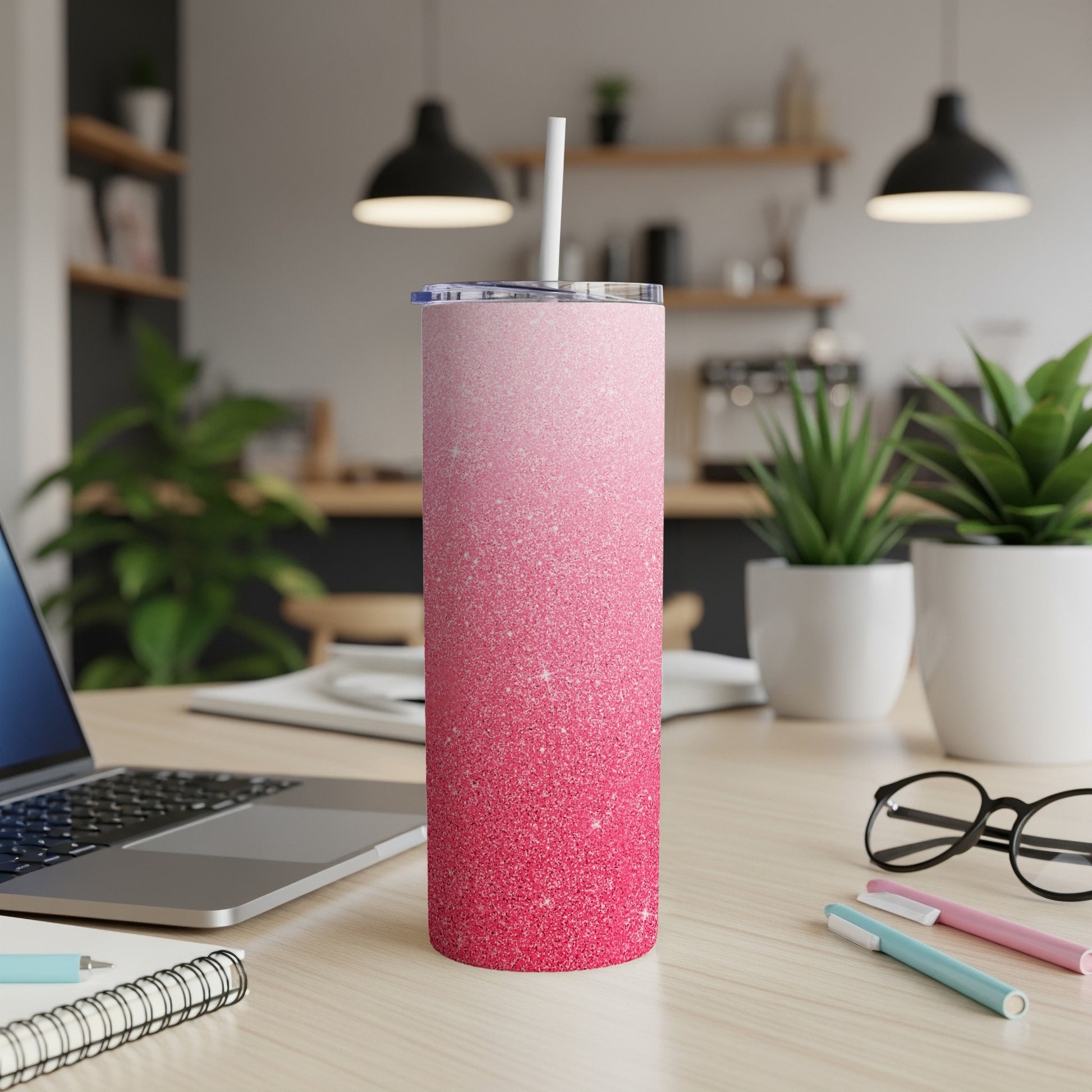 Pink glitter tumbler with straw on a desk with a laptop and pens.