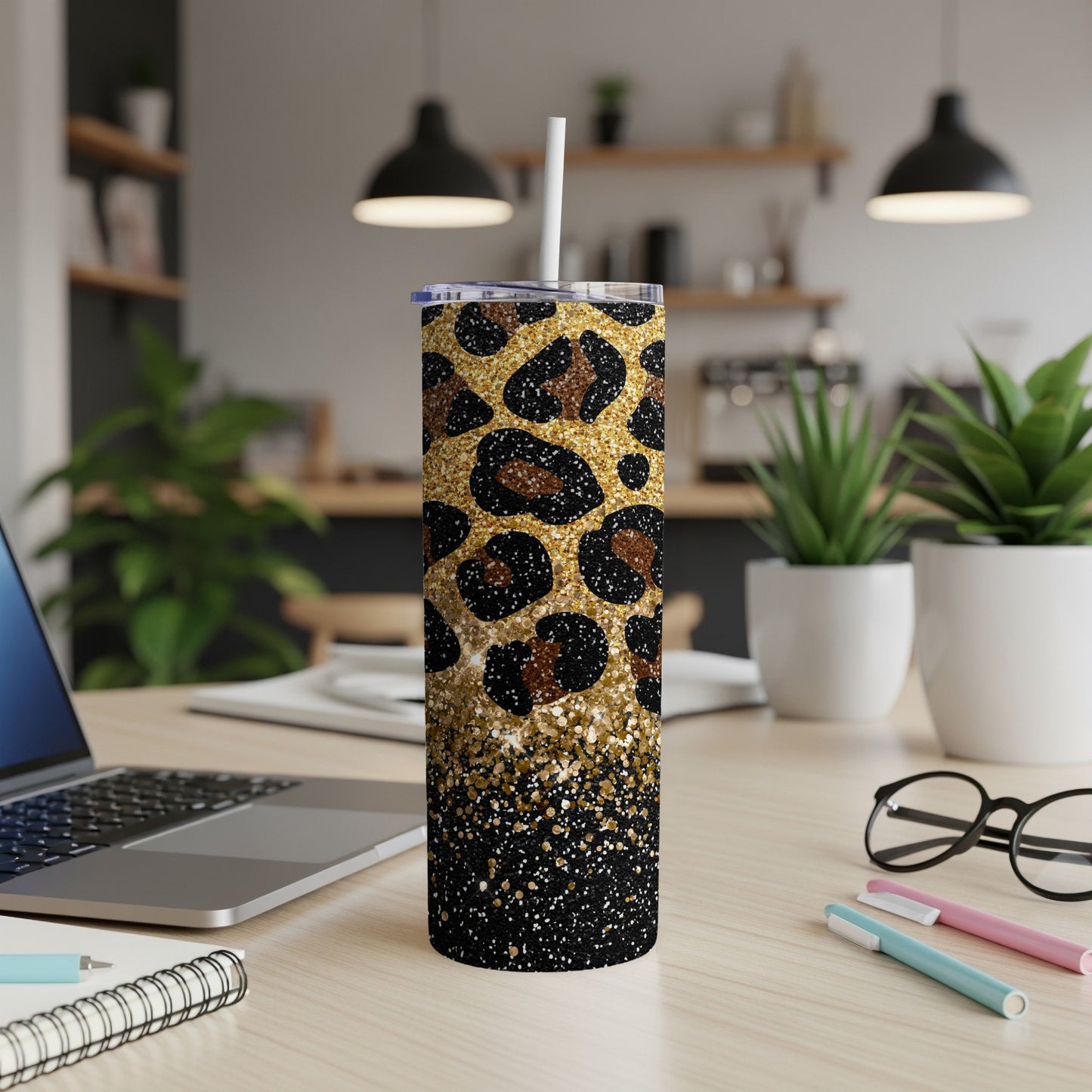 Leopard print and gold glitter tumbler with straw on a desk.