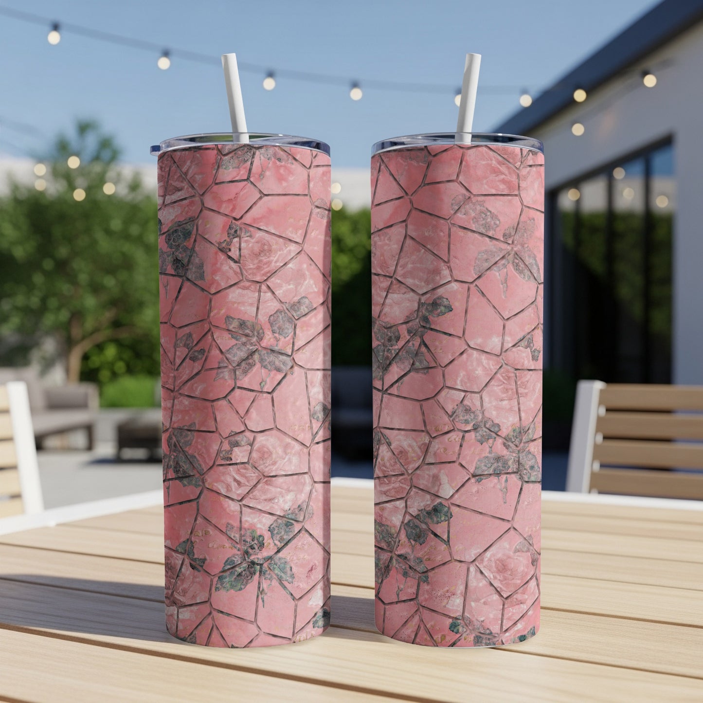 Two pink floral patterned tumblers with straws sit on a wooden table.