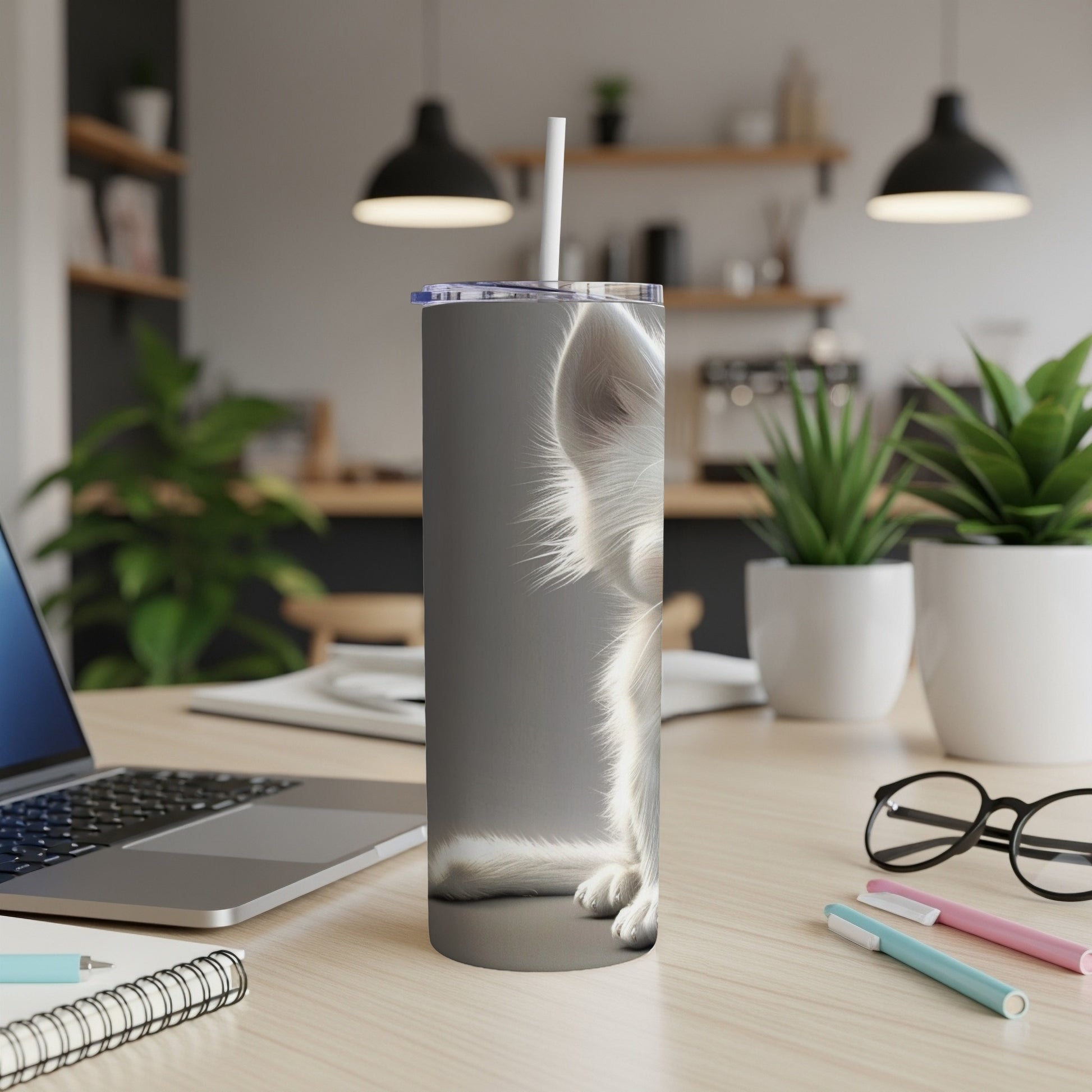 White fluffy cat on a gray tumbler with a straw, on a desk.