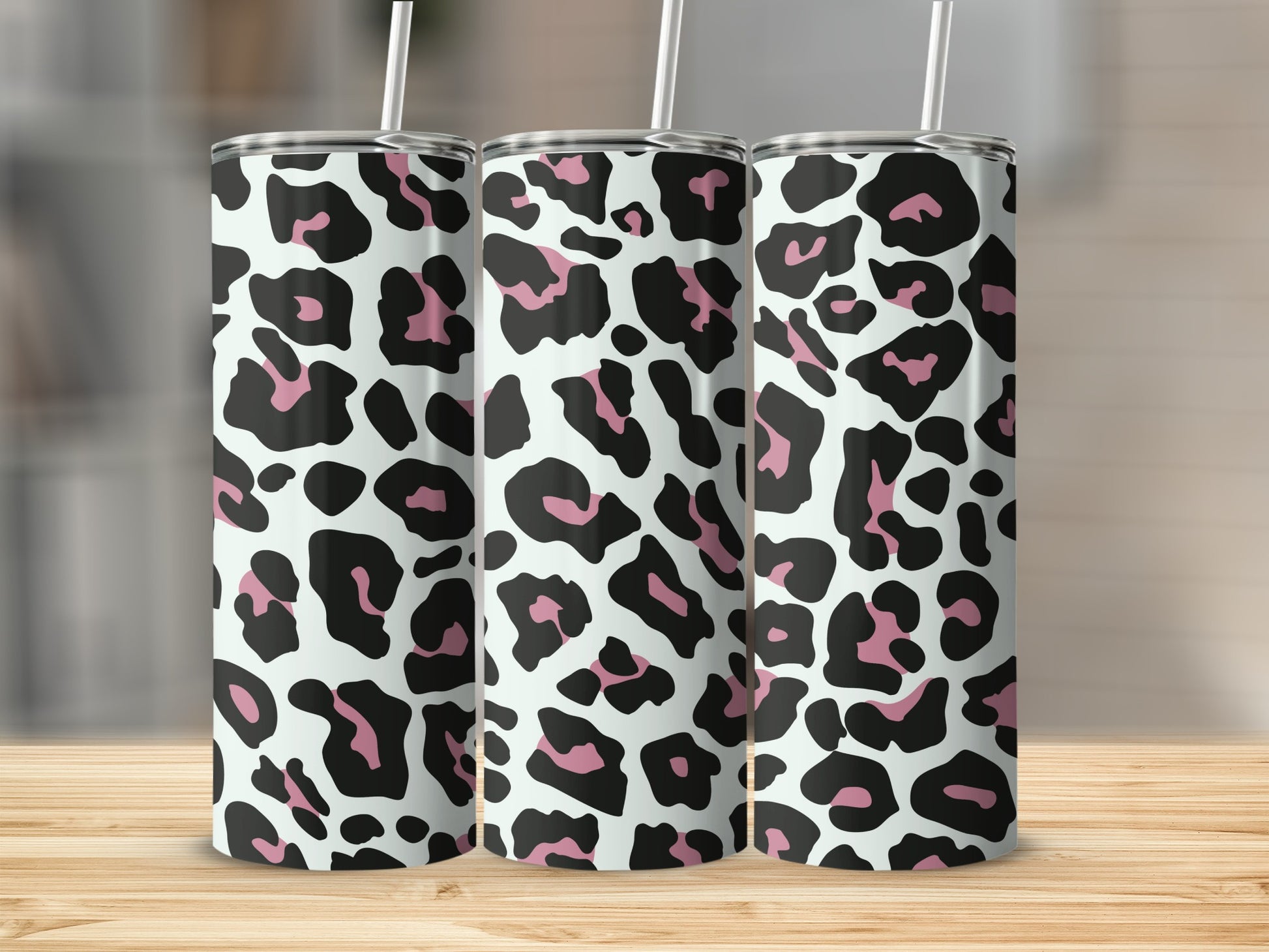 Three tumblers with a black, pink, and white leopard print pattern stand on a wooden surface.