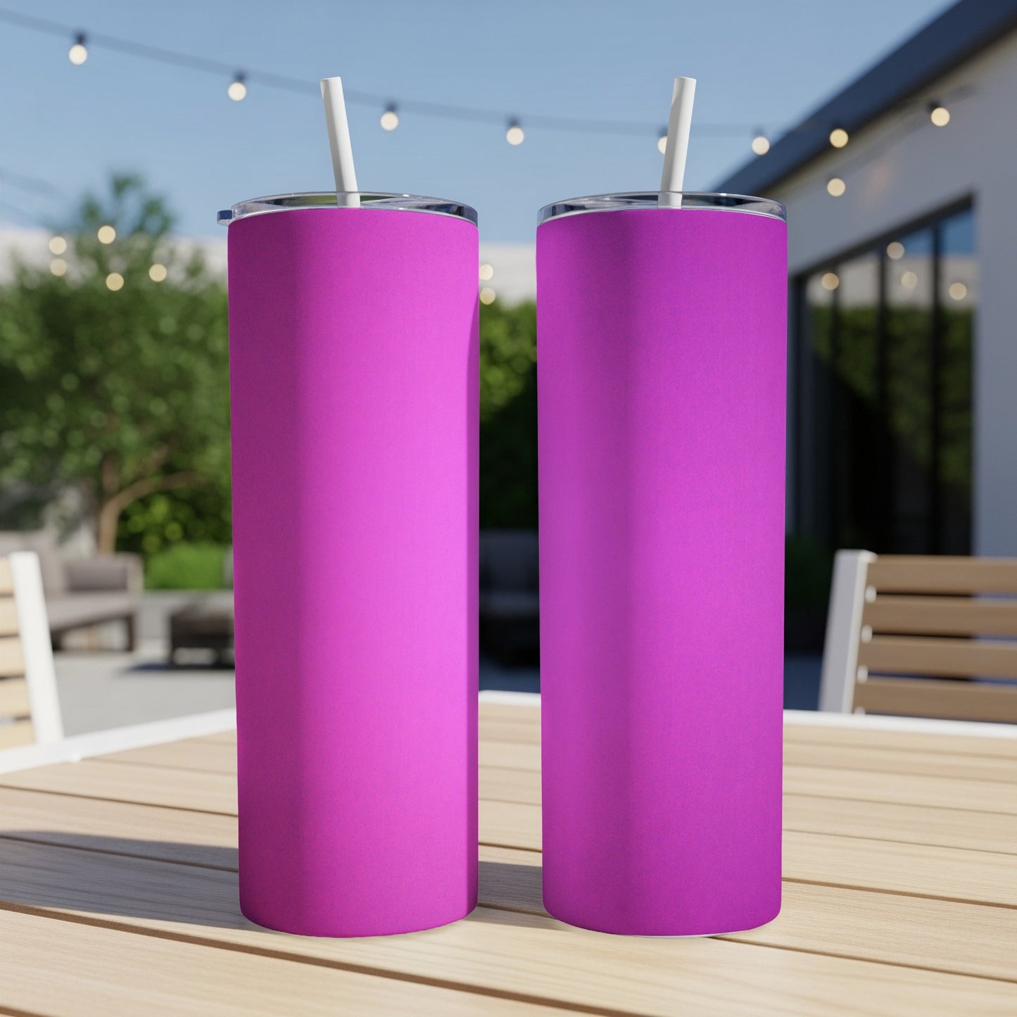 Two pink tumblers with straws sit on a wooden table outdoors.