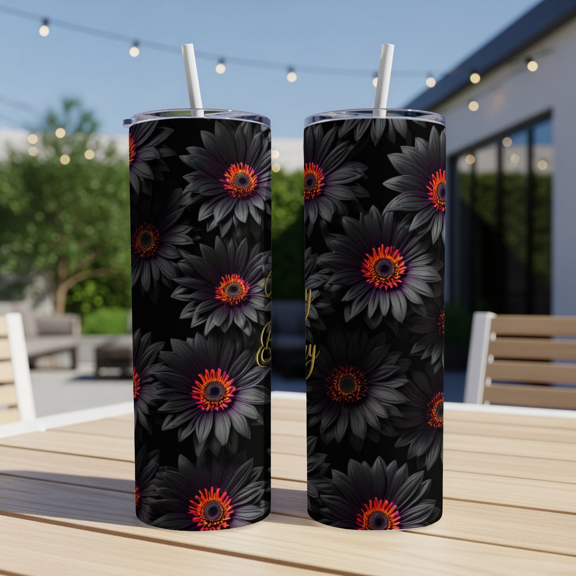 Black floral tumbler with straw on outdoor table.