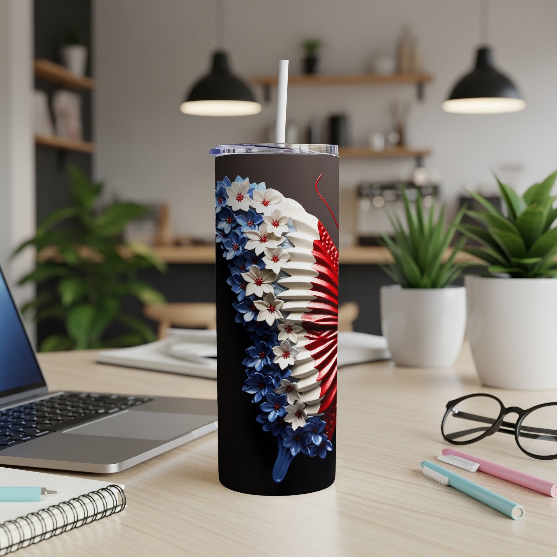Black tumbler with red, white, and blue floral design, on a desk with laptop and pens.