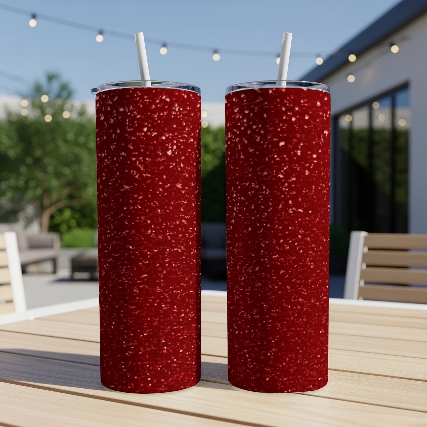 Two red glitter tumblers with white straws on a wooden table outdoors.