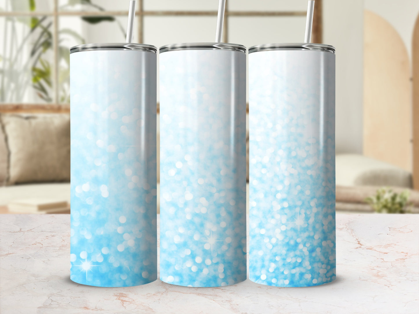Three blue glitter ombre tumblers with straws on a marble countertop.