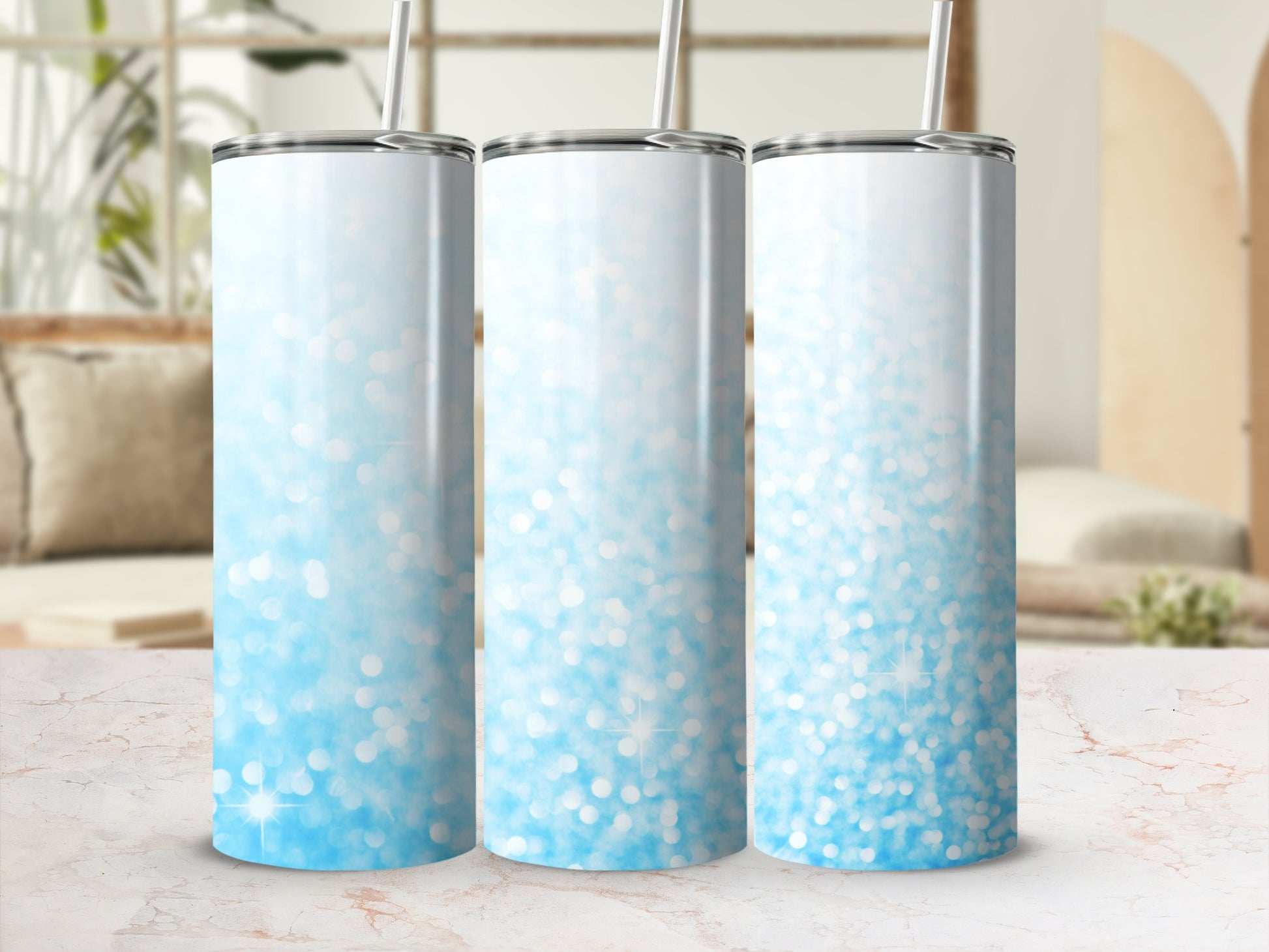 Three blue glitter ombre tumblers with straws on a marble countertop.