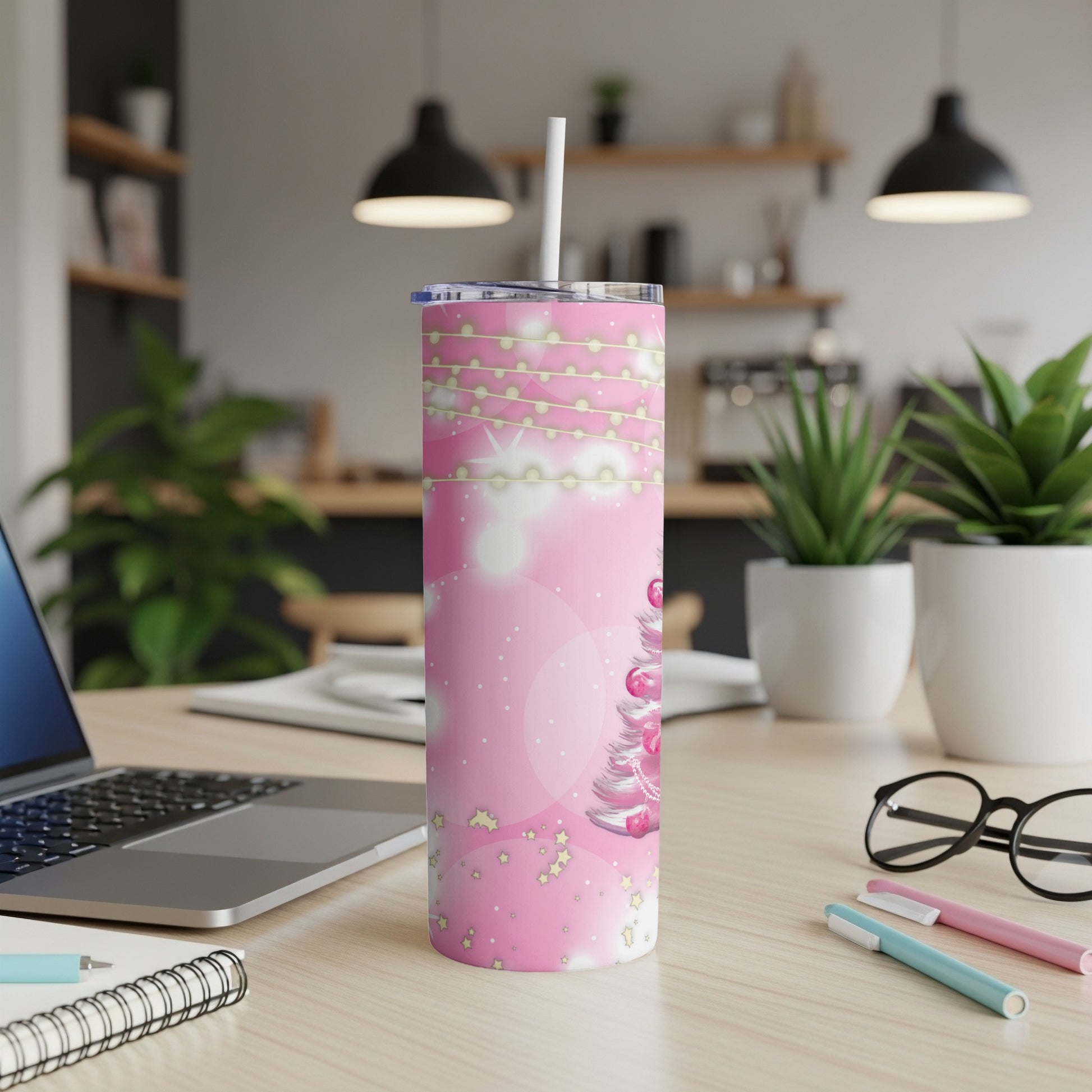 Pink tumbler with Christmas tree and lights on a desk.