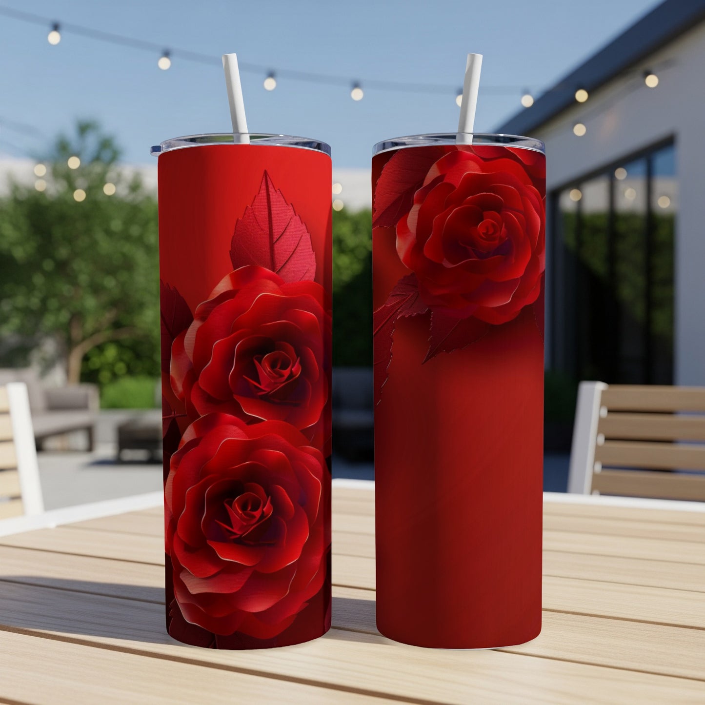 Red rose patterned tumbler with straw on a wooden table outdoors.
