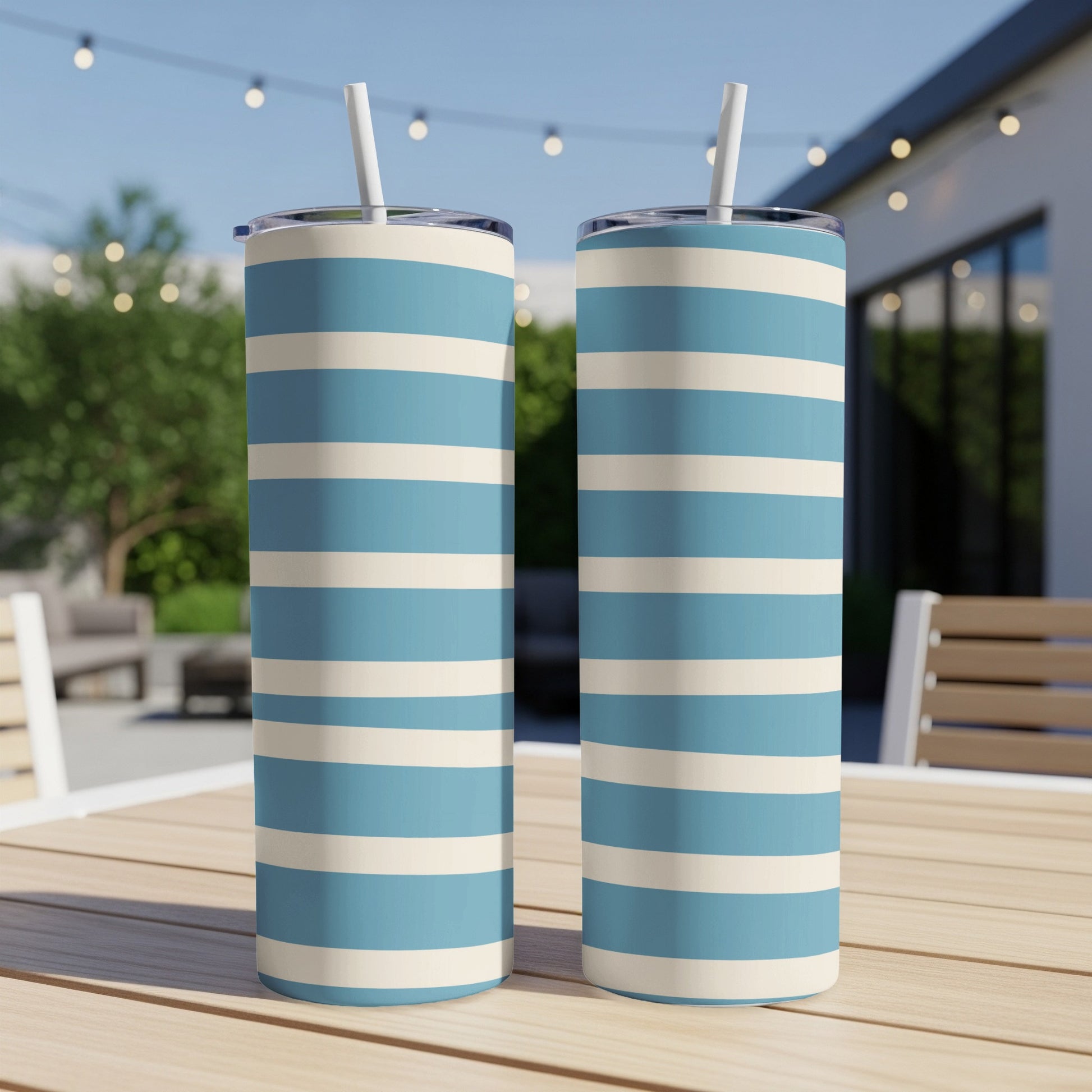 Two tall striped tumblers in blue and cream with white straws on a table.