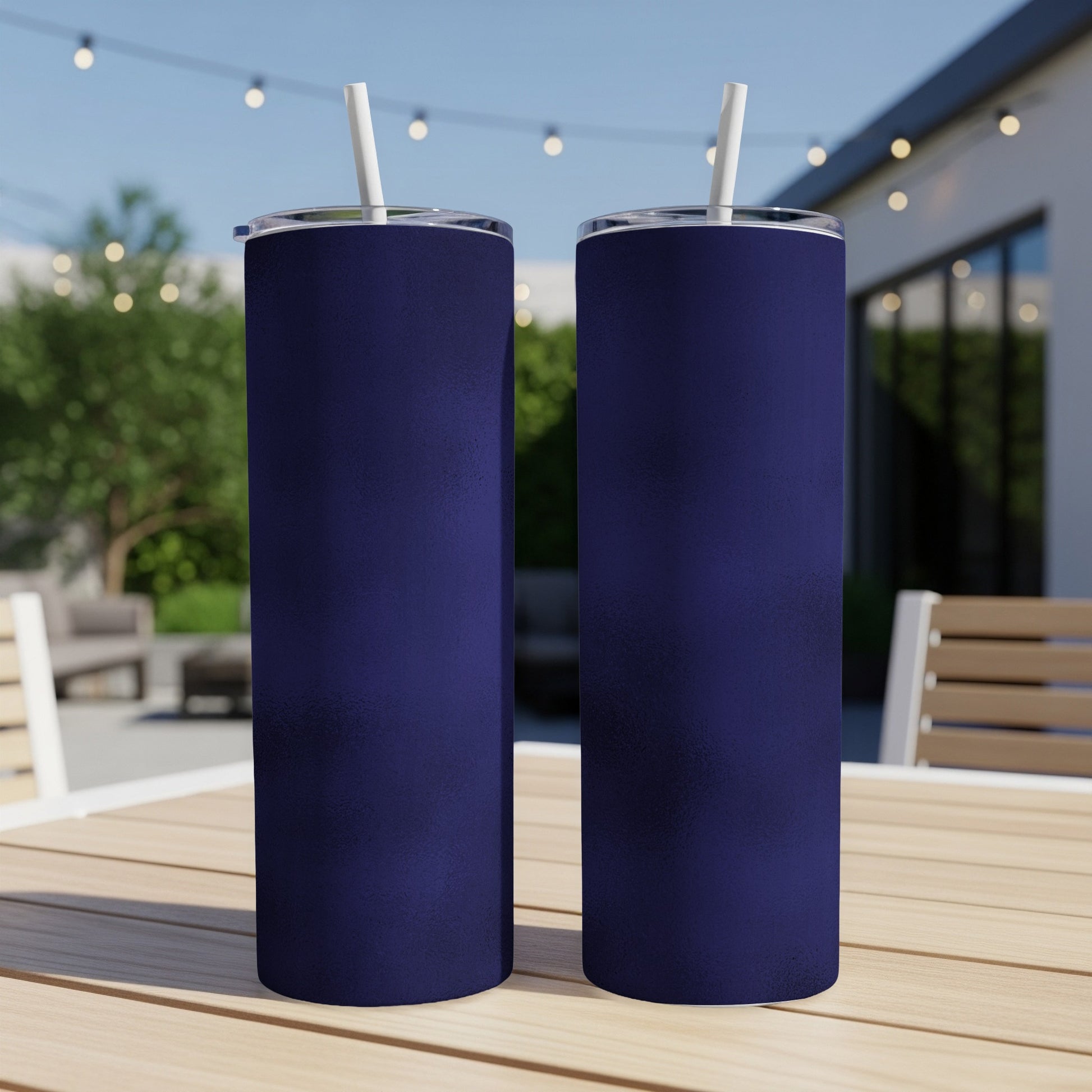 Two dark blue tumblers with white straws stand on a wooden table outdoors.