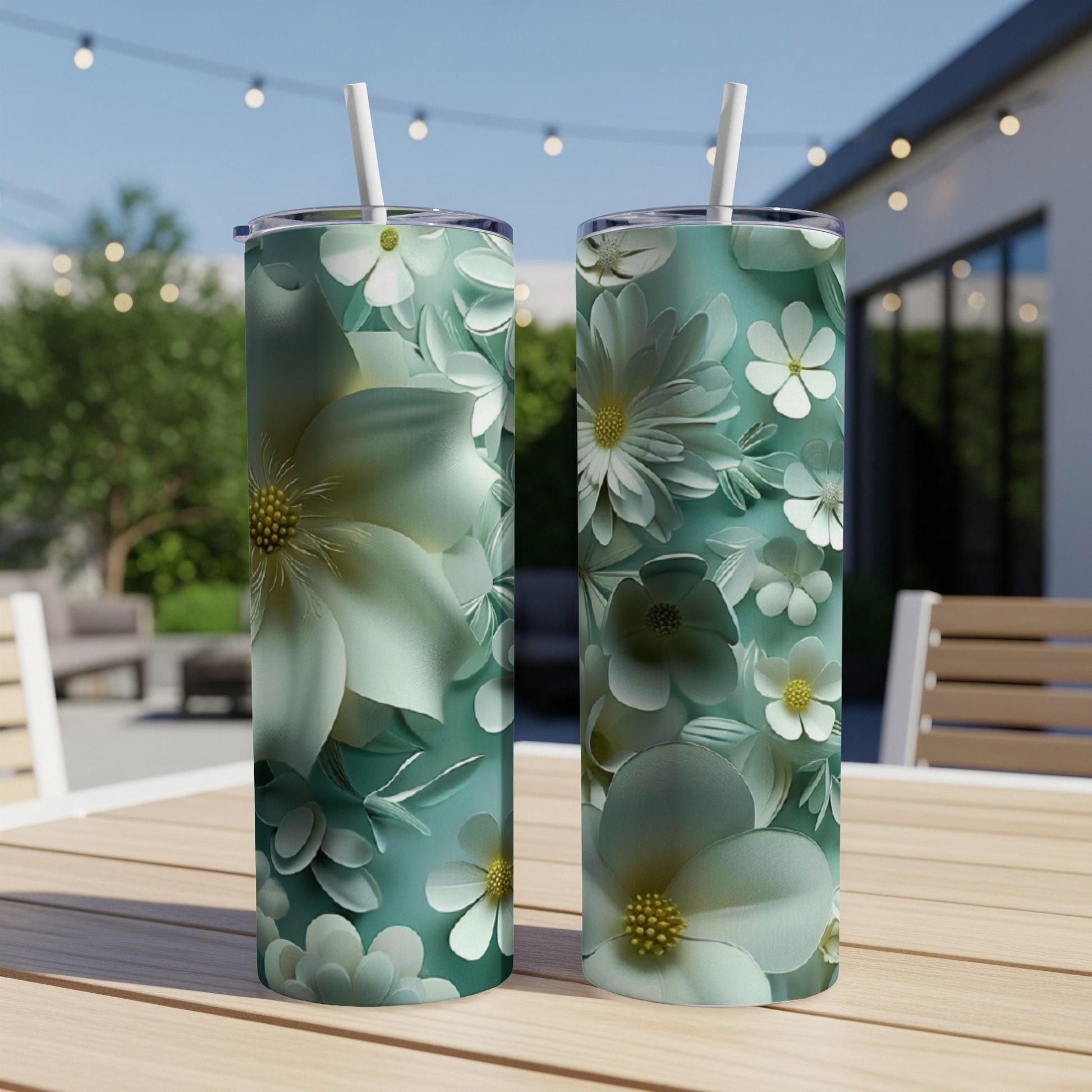 Two teal tumblers with embossed white and green floral designs sit on a table.