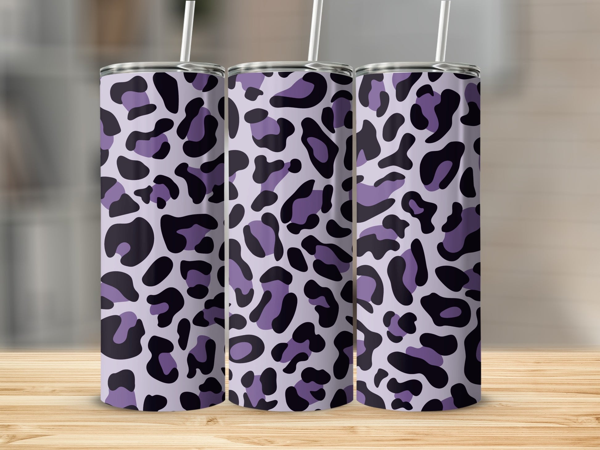 Three purple and black leopard print tumblers with straws stand on a wooden surface.