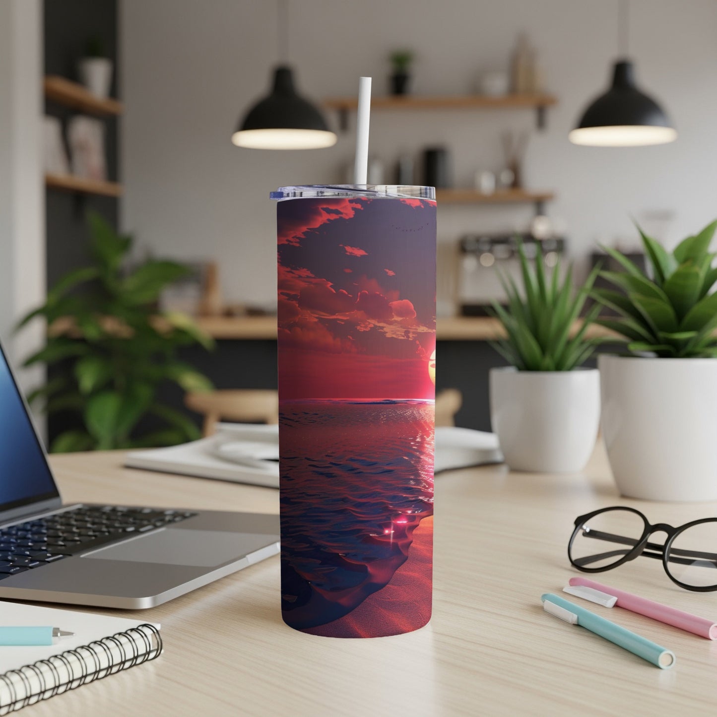 Tumbler with a sunset over the ocean, beach sand, and laptop.