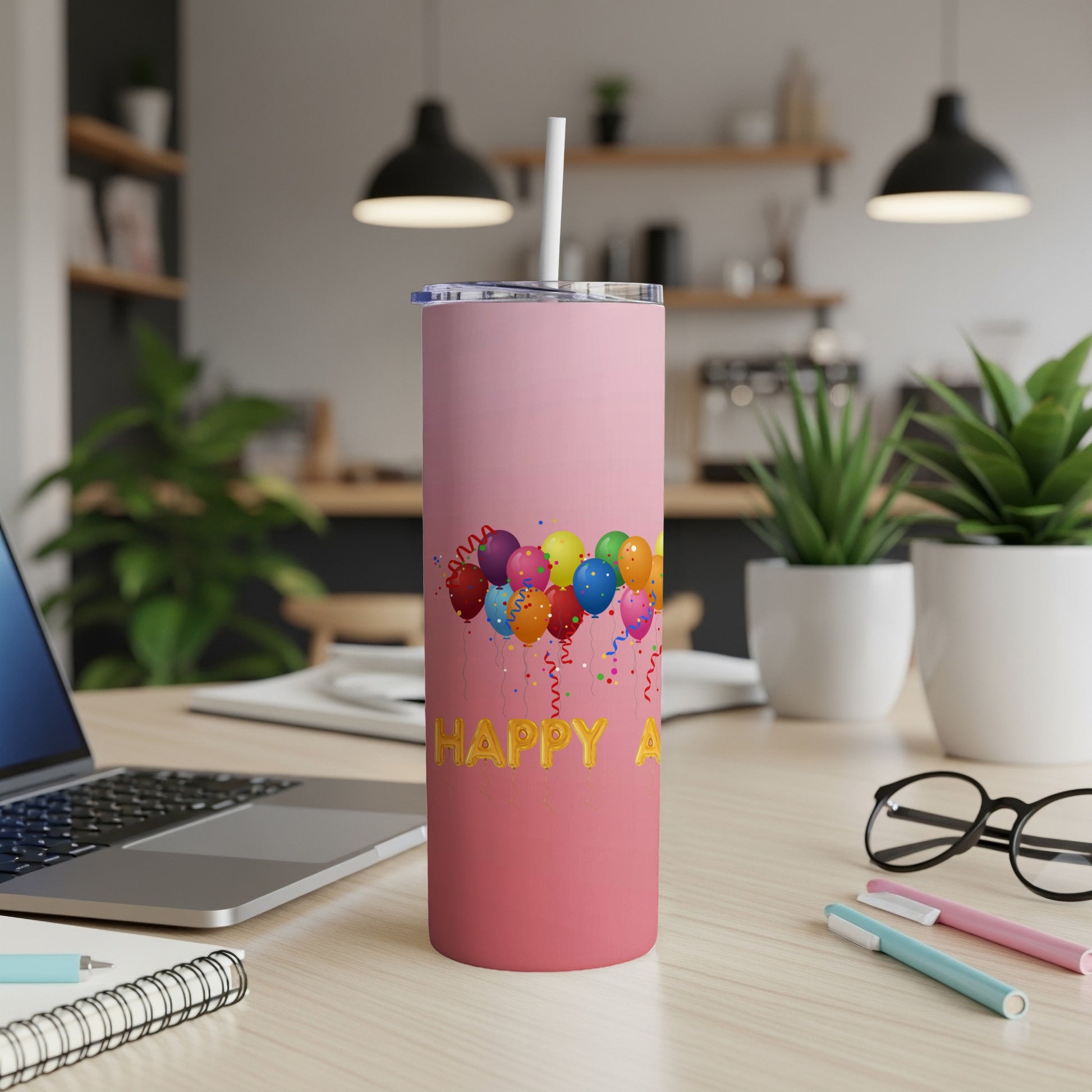 Pink tumbler with colorful balloons and "Happy A" text on a desk.