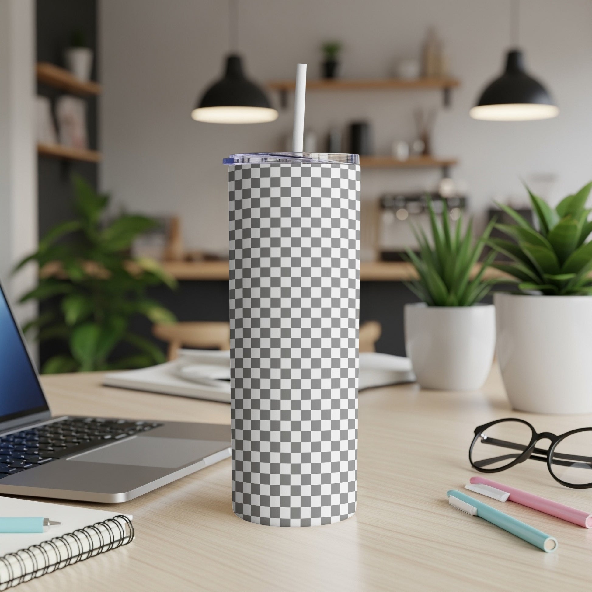 Checkerboard pattern tumbler with straw on desk next to laptop.