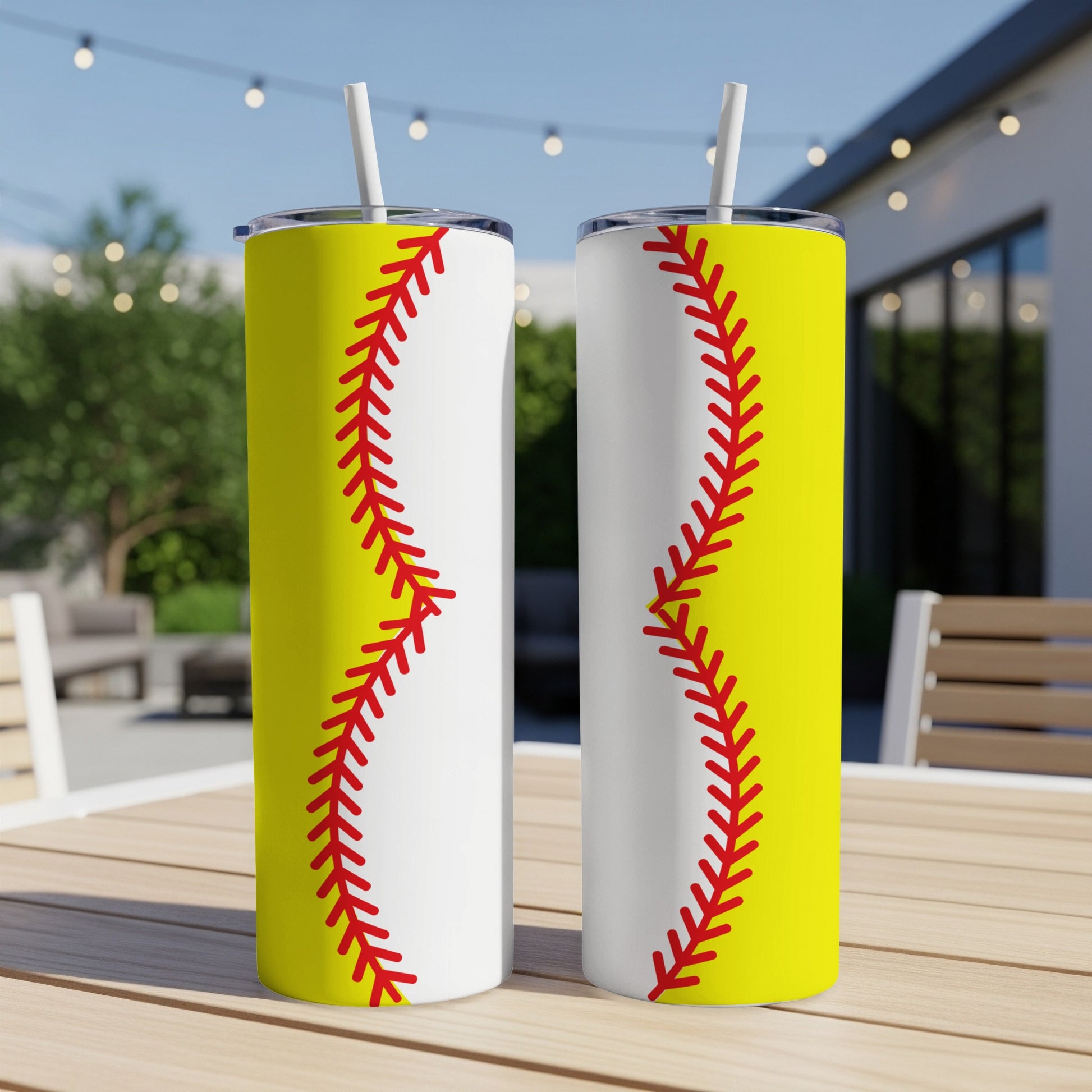 Two white and yellow softball-themed tumblers with red stitching stand on a table.