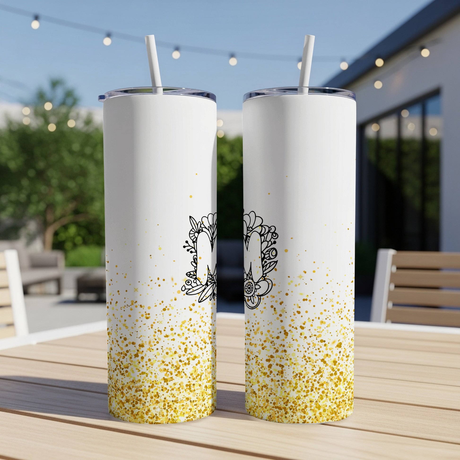 Two white tumblers with gold glitter and a floral letter "M" design.