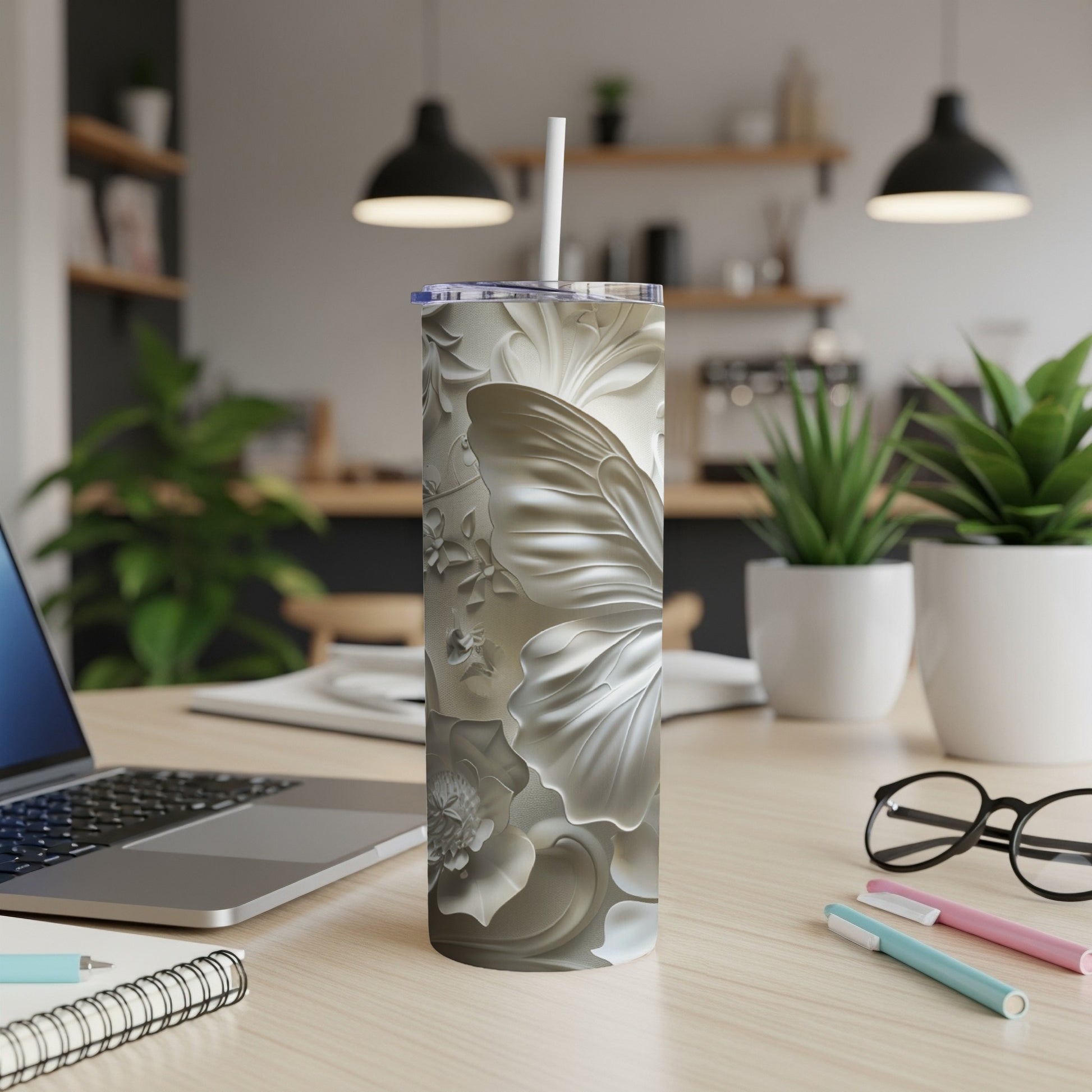 Silver floral tumbler with white lid and straw on a desk.